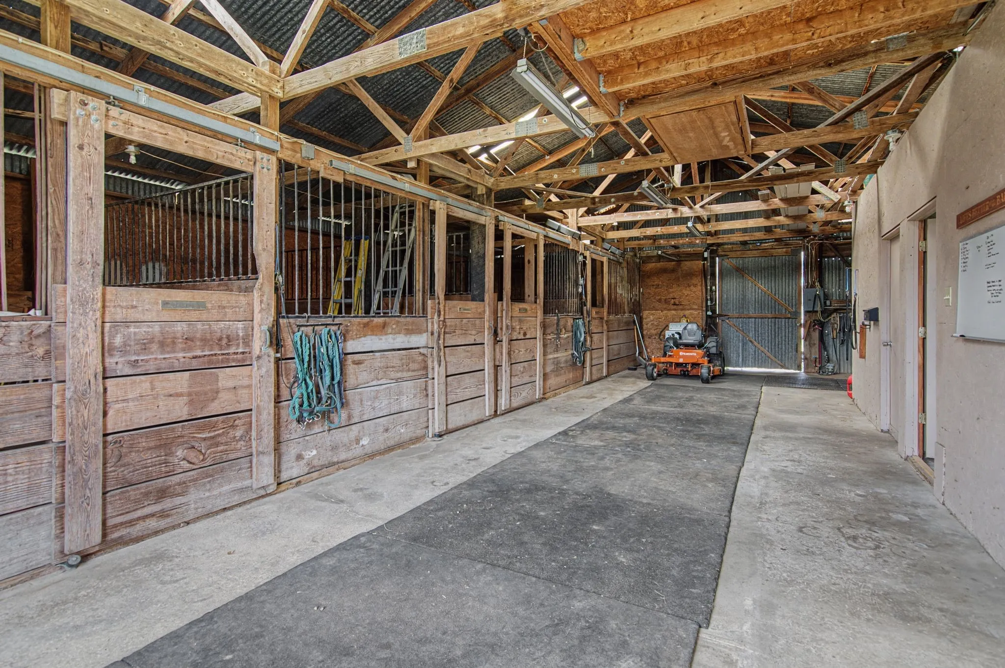 Barn structure with exposed wood framing, multiple stalls with individual entries, and a corrugated metal roof