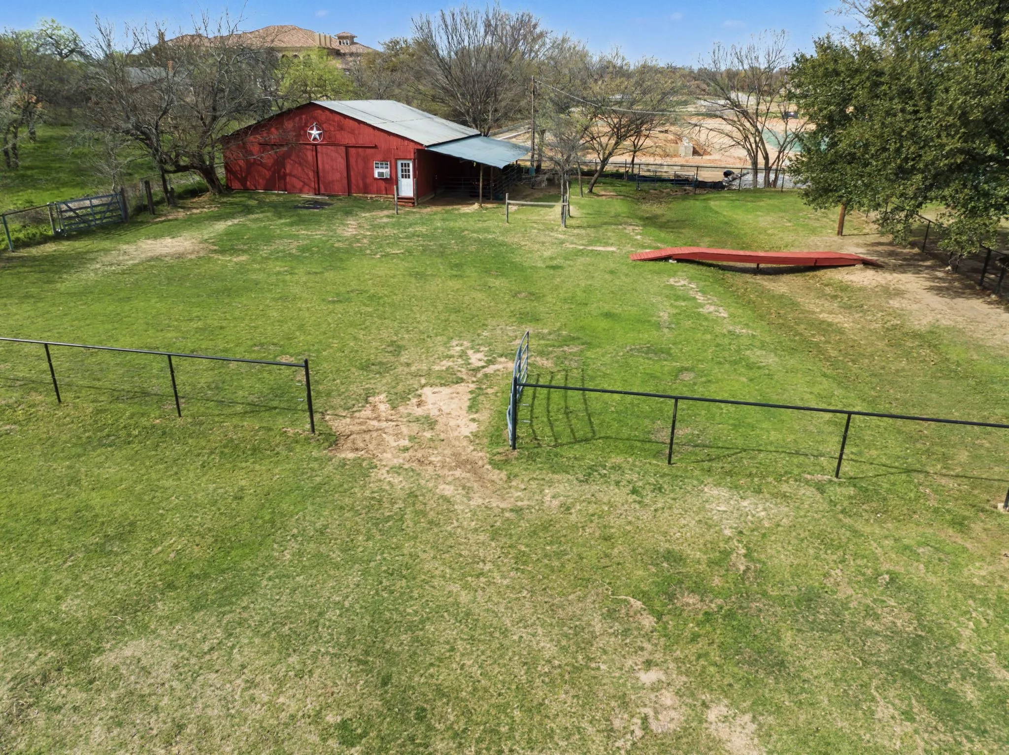 Expansive grassy outdoor space featuring a red barn with a white star accent, a covered lean-to, and partial black fencing
