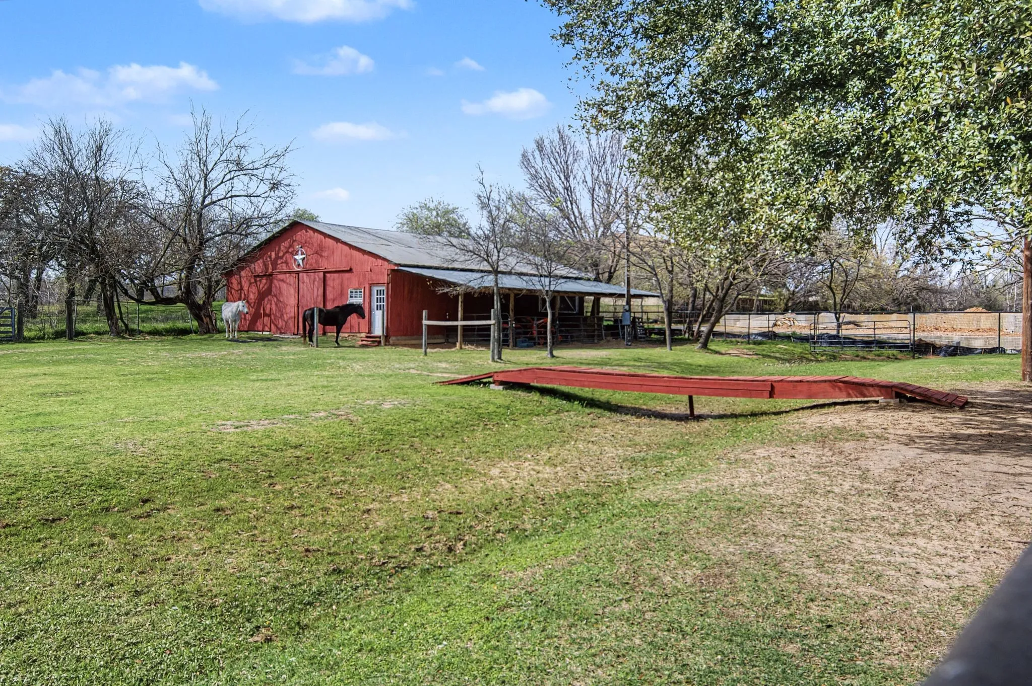 Red barn structure with a prominent white cross accent, featuring an attached covered lean-to area, a corrugated metal roof, and a visible side entry door