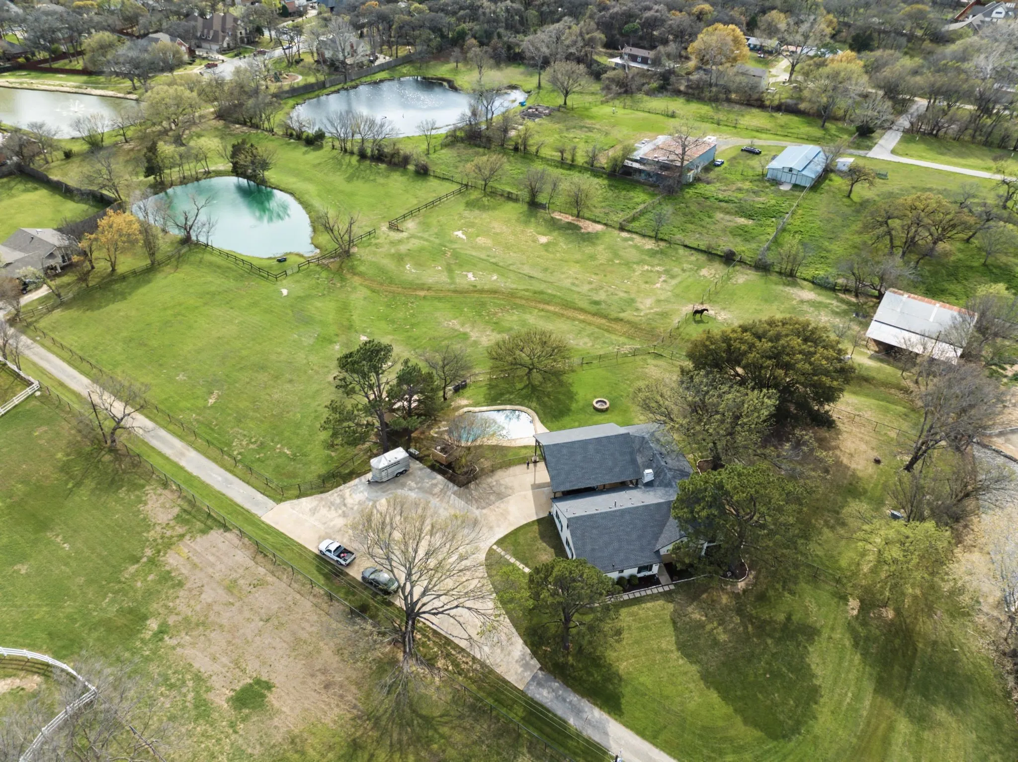 Expansive grounds featuring multiple ponds, mature trees, a private driveway, and a residential structure with an attached garage