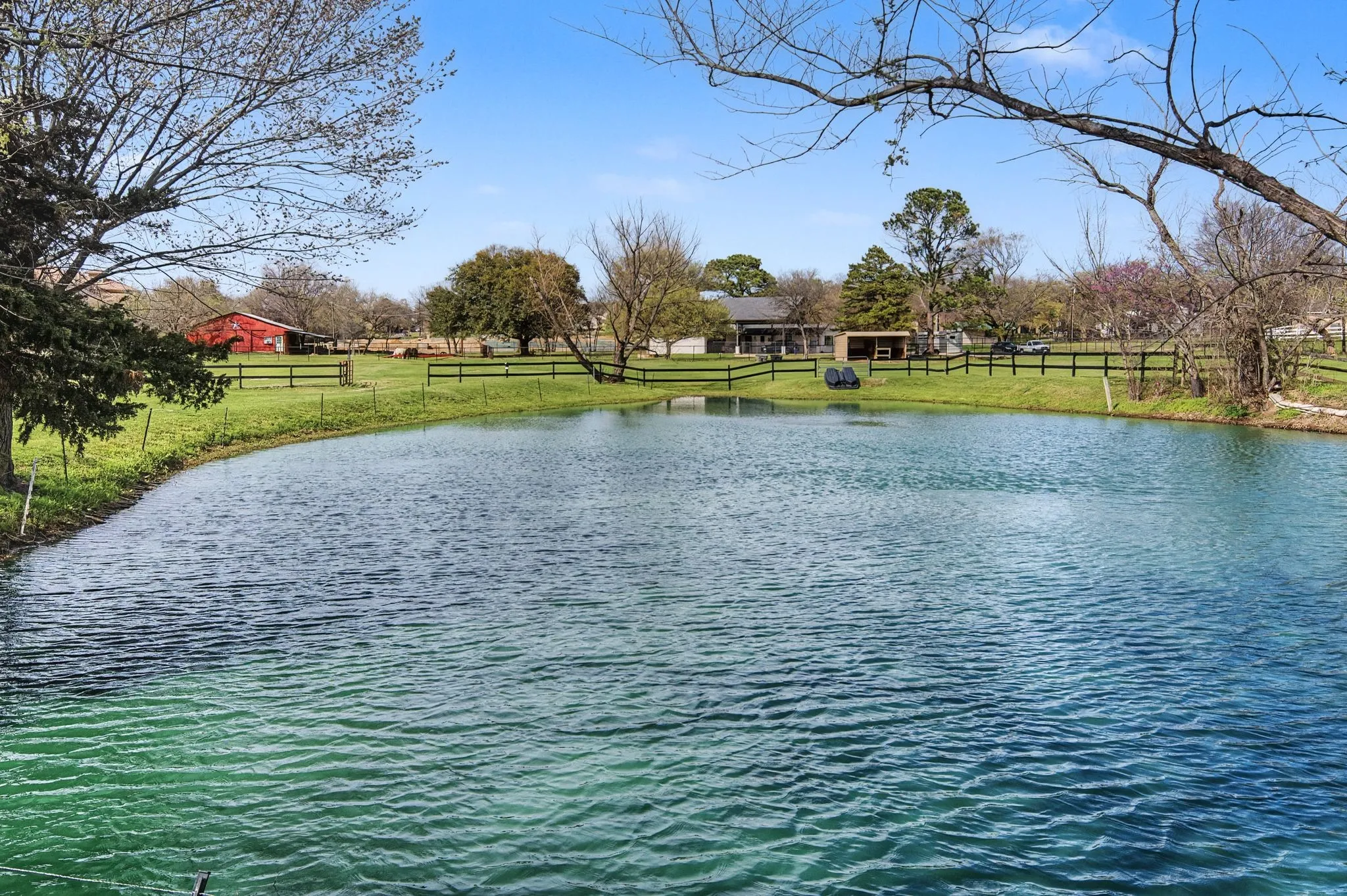 Water feature with surrounding green landscape, bordered by a black fence and mature trees