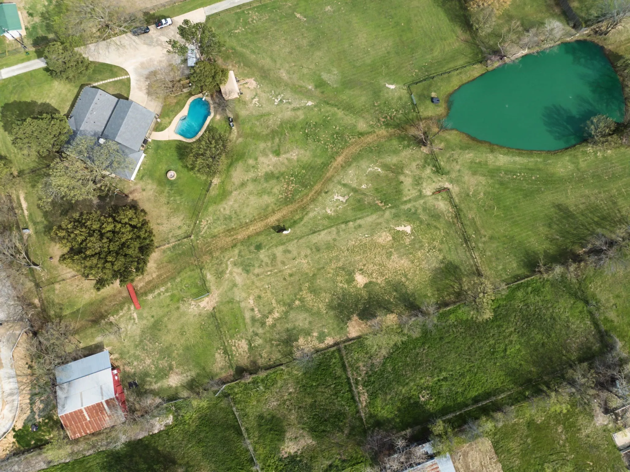 Expansive acreage featuring a single-story residence with a gabled roof, an in-ground swimming pool, a private pond, and a detached barn
