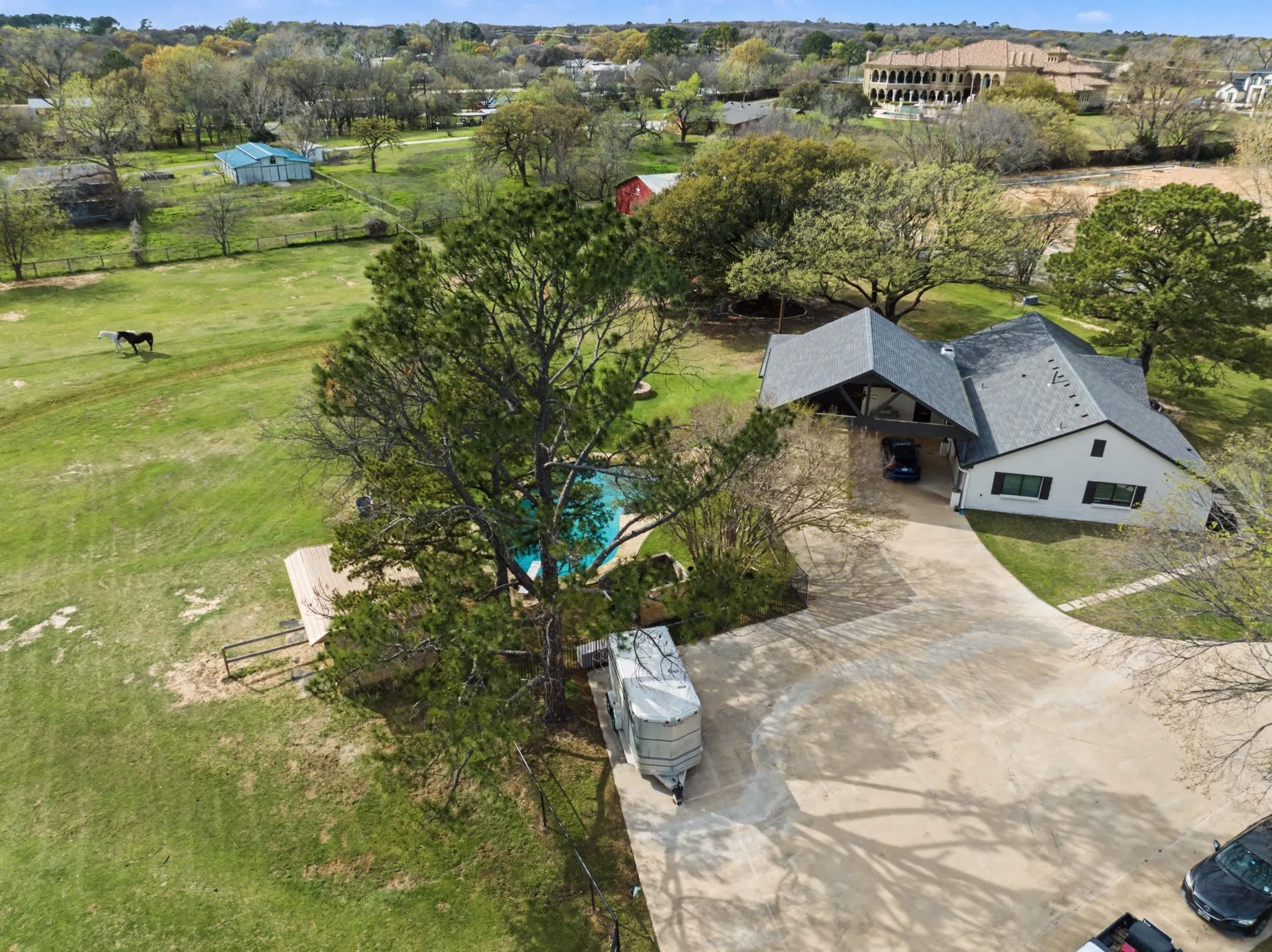 Expansive property featuring a large residence with a dark gray roof, a circular driveway, and a swimming pool
