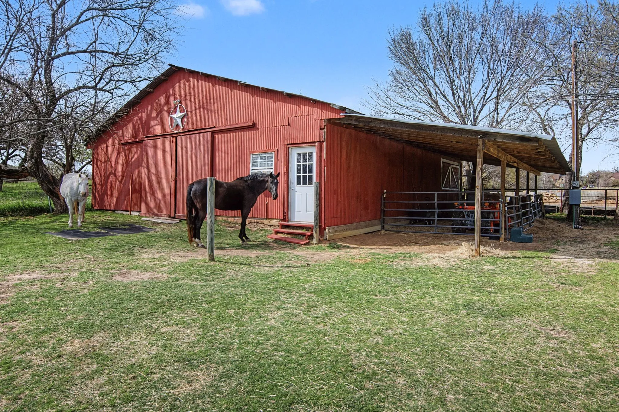 Red barn structure featuring a metal roof, sliding barn doors, an attached covered lean-to, and perimeter fencing