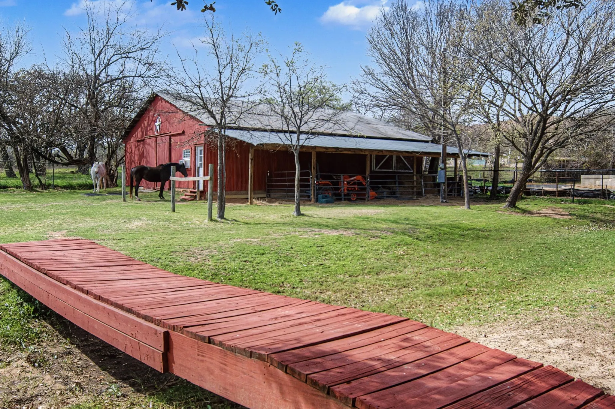 Red wood-sided barn with white trim, metal roof, and an attached covered lean-to structure