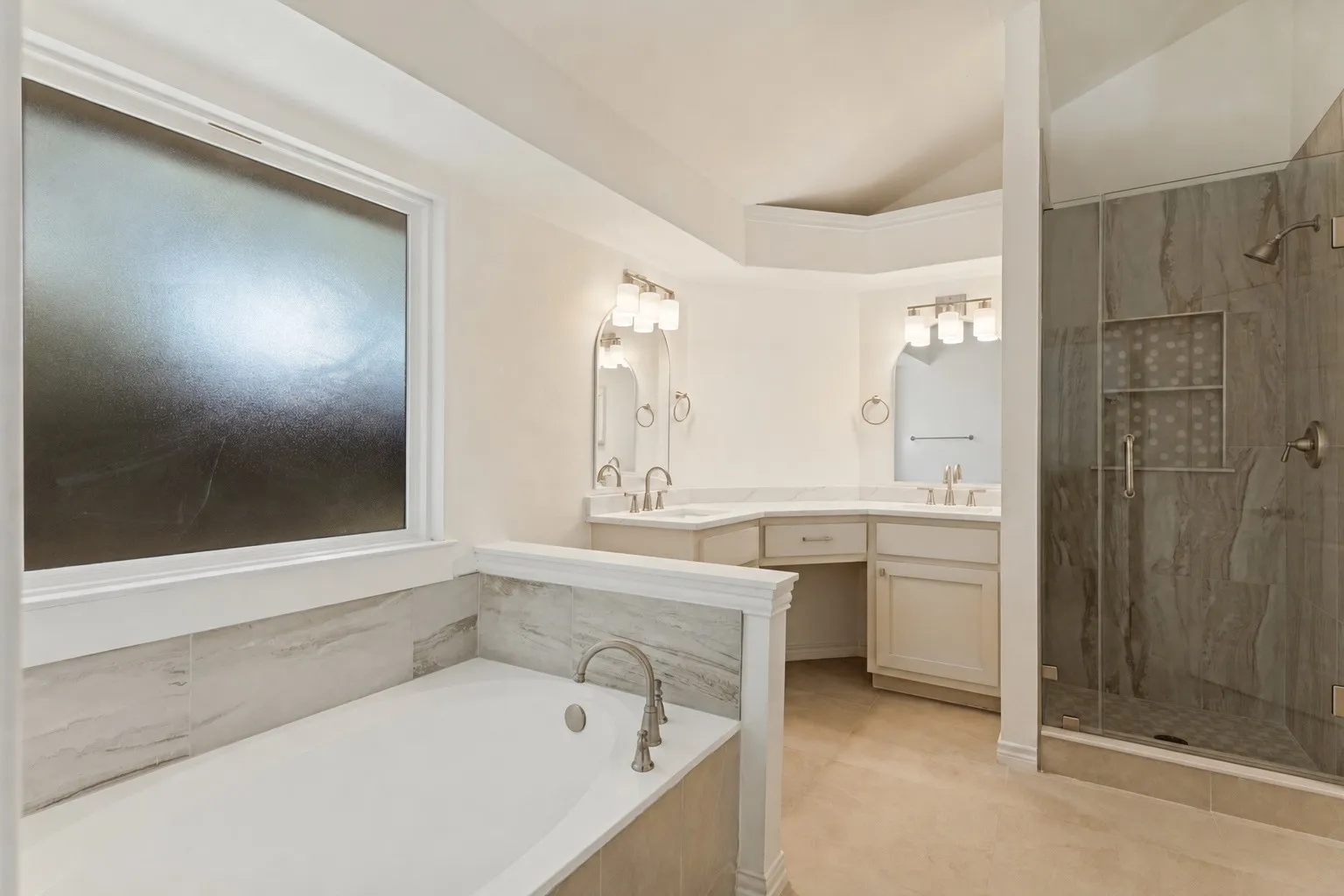 Recessed soaking tub, expansive dual vanity, separate glass-enclosed shower, tile flooring, and vaulted ceiling