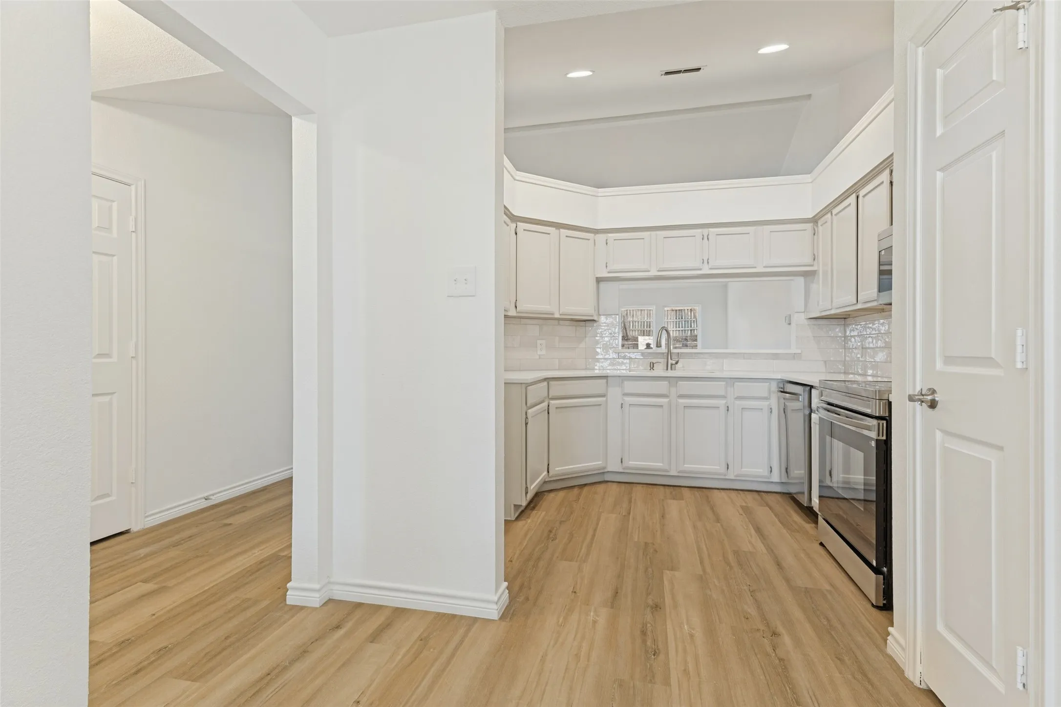 Kitchen featuring light wood-finish flooring, white cabinetry, integrated stainless steel appliances, a tile backsplash, and recessed lighting
