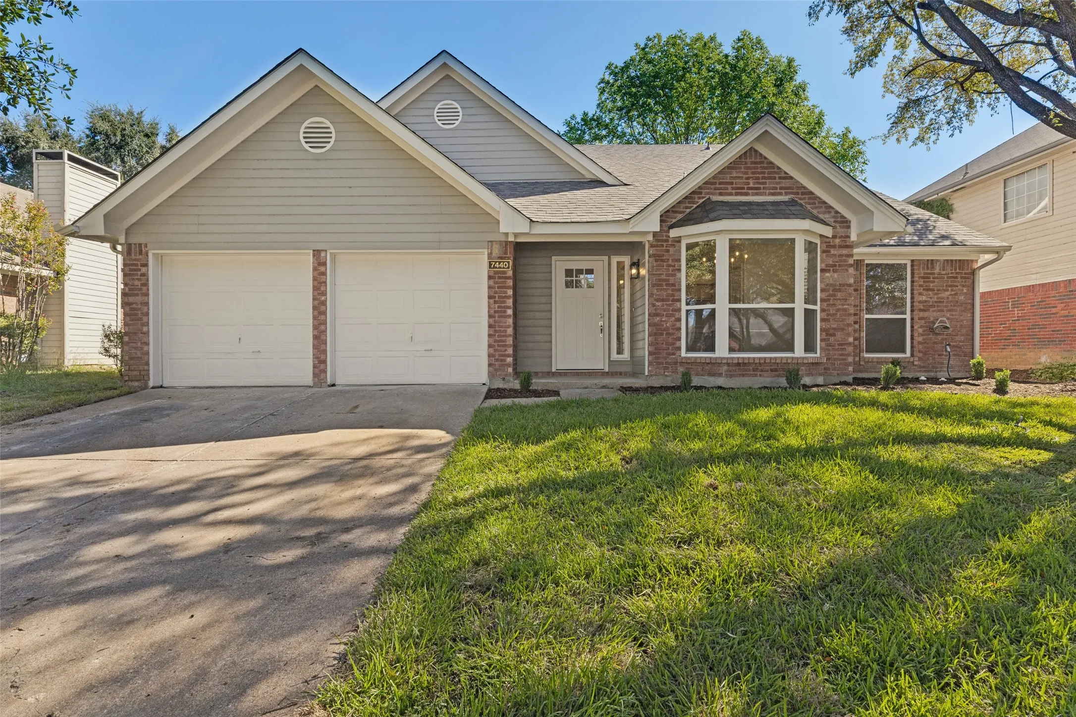 Brick and siding exterior featuring a two-car garage, bay window, and gabled roofline