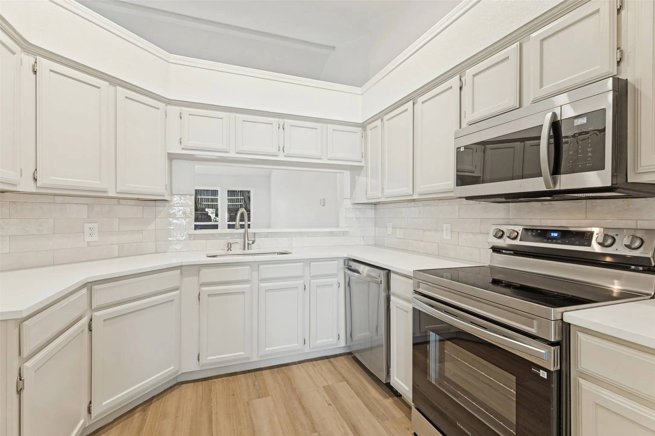 White cabinetry, stainless steel appliances, light-toned backsplash, light-toned countertops, and wood-finish flooring