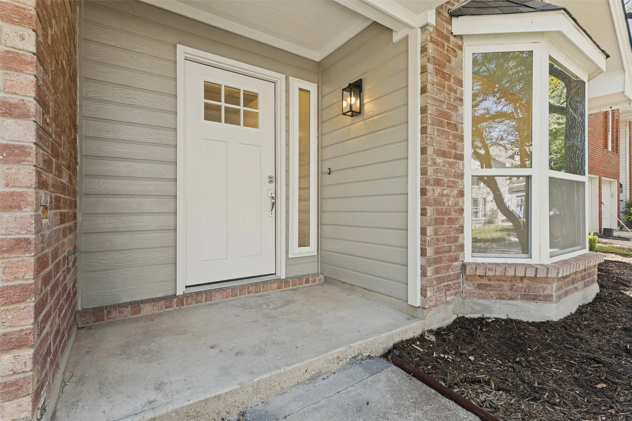Brick and siding exterior with a paneled entry door, transom sidelight, and an exterior wall lantern