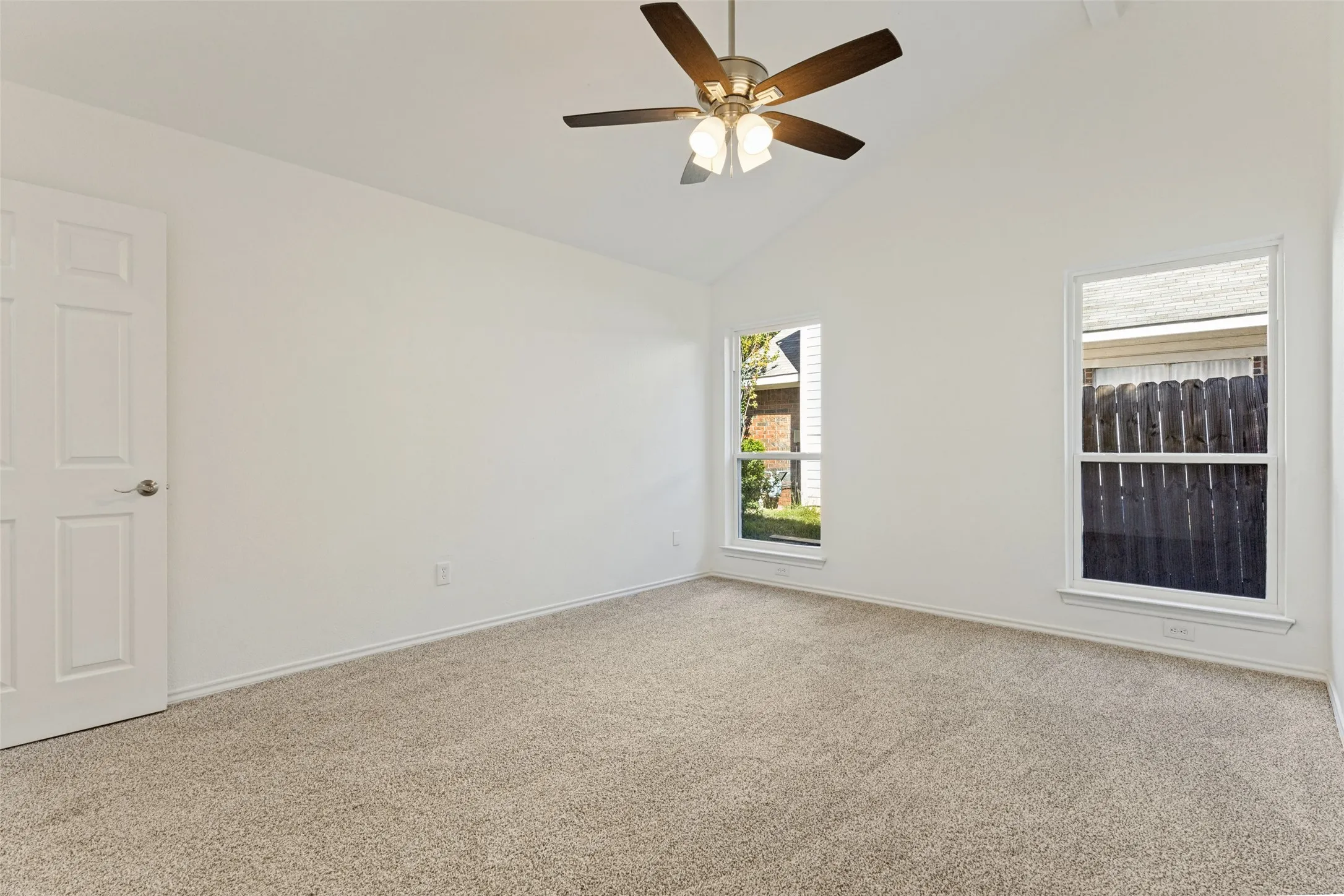 Vaulted ceiling, ceiling fan with light fixture, two windows, carpet flooring, and a paneled door