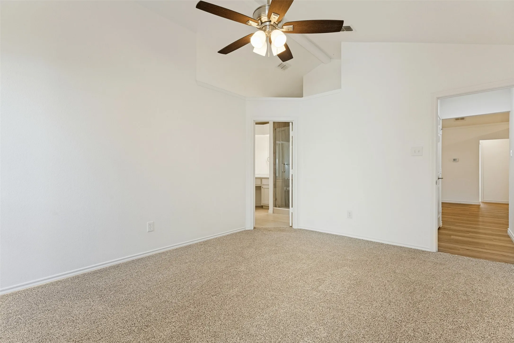 Vaulted ceiling with an integrated ceiling fan, light-toned carpeting, and white painted walls