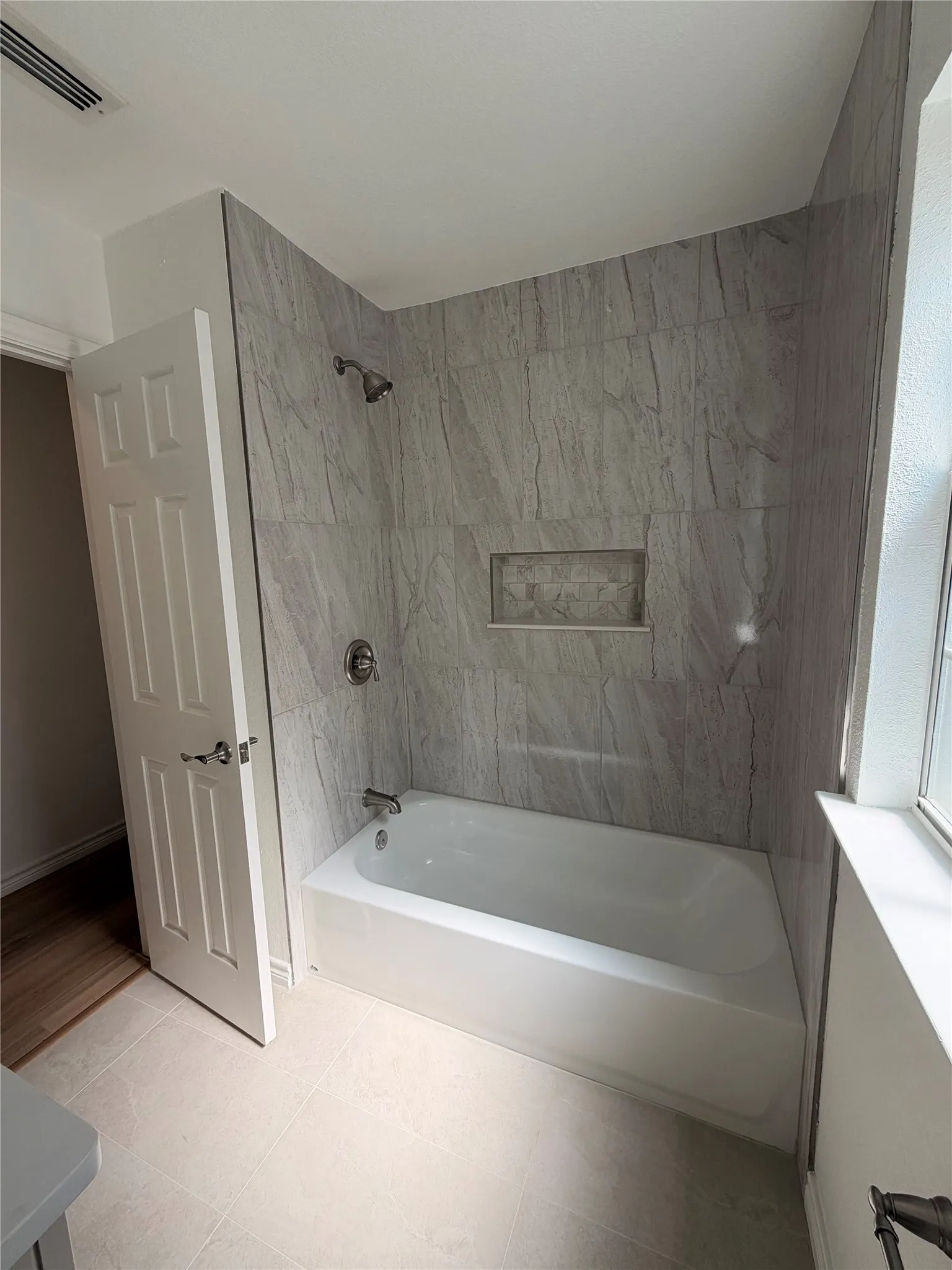 Bathtub shower with light-toned wall tile, recessed shower niche, and brushed nickel fixtures