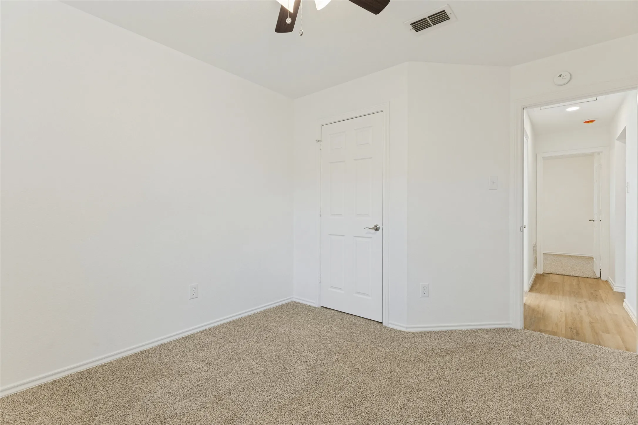 Neutral wall finishes, carpet flooring, a ceiling fan with integrated lighting, and a paneled door with a lever handle