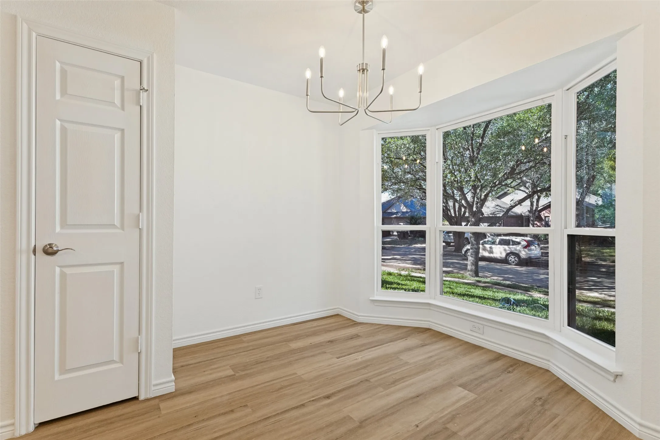Bay window with exterior scenery, wood-finish flooring, contemporary chandelier, and a paneled interior door