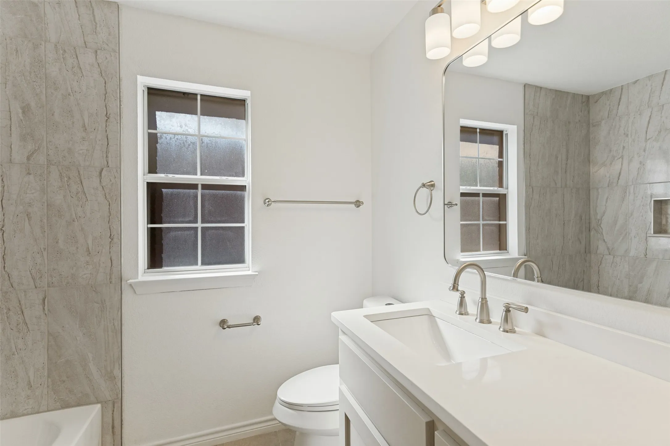 White vanity with integrated sink, brushed nickel faucet, large wall mirror, and modern lighting fixture