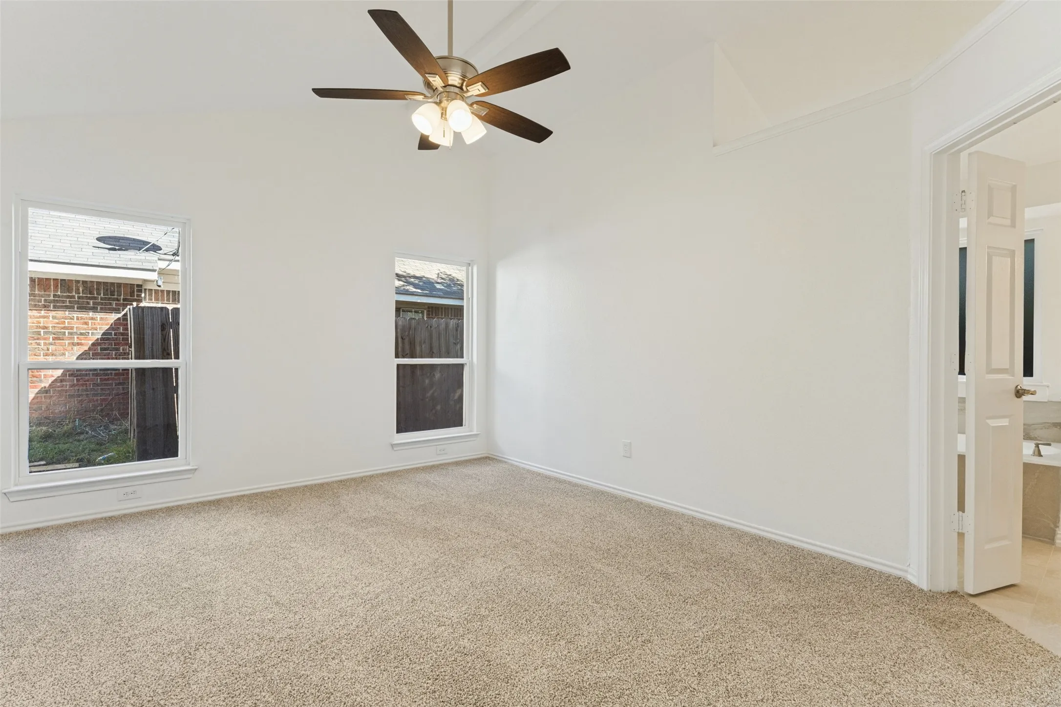 Carpeted room featuring a vaulted ceiling with a ceiling fan, two windows, and direct access to a tiled bathroom