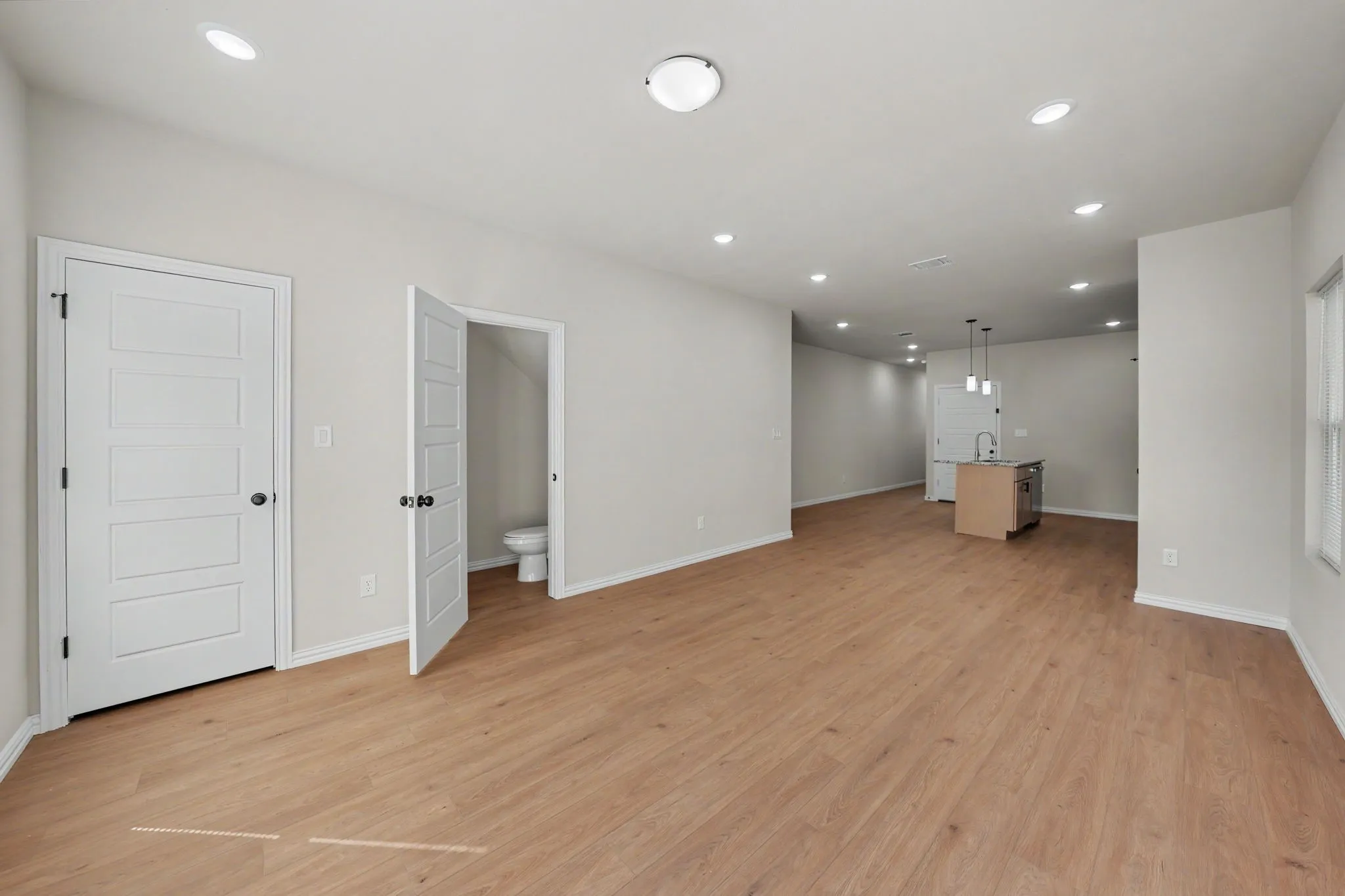 Expansive open-concept living space with wood-finish flooring, recessed lighting, and a modern kitchen island with pendant lighting and built-in sink