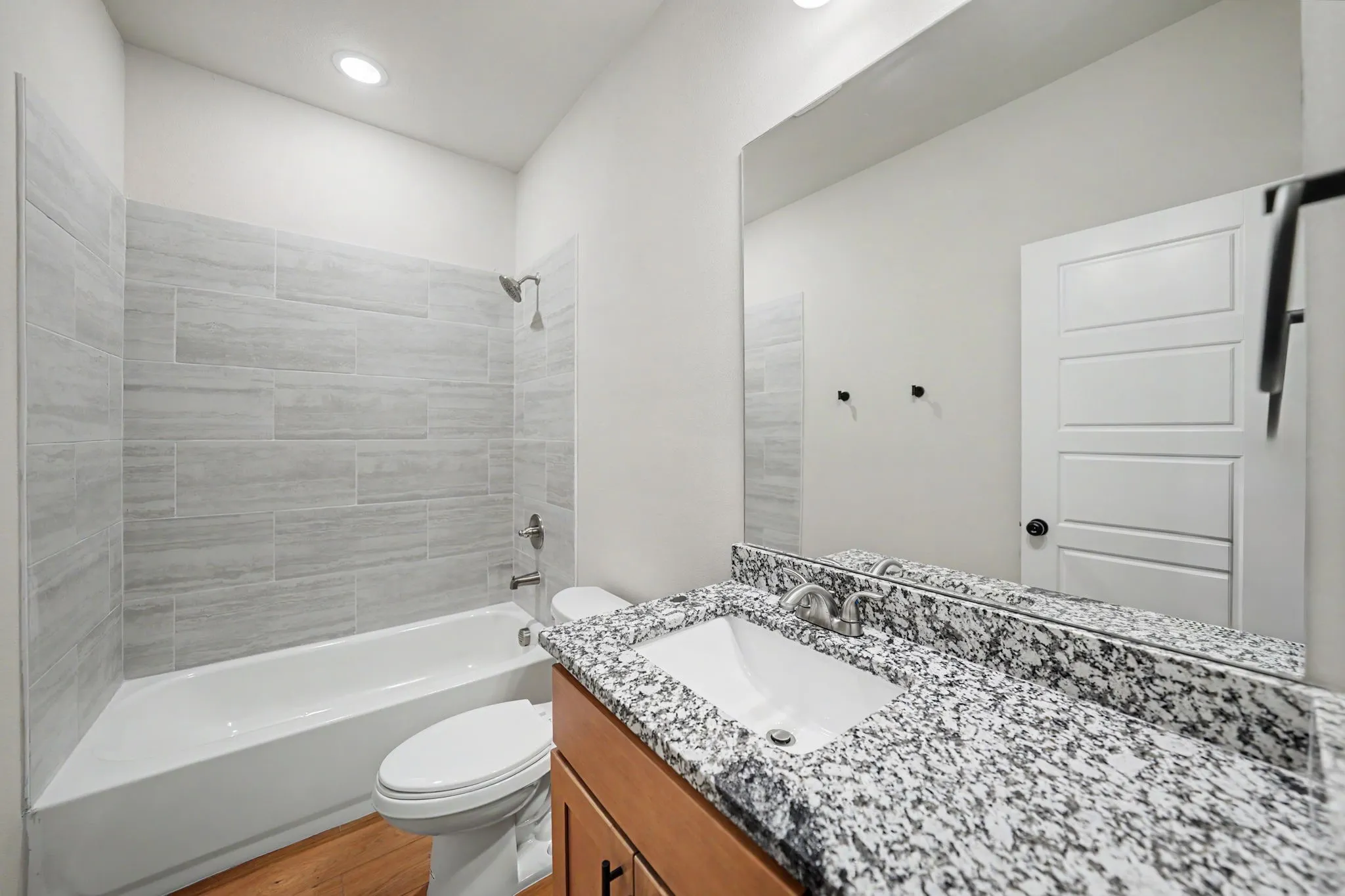 Bathroom featuring a single vanity with stone countertop, integrated sink, wood-finish cabinetry, and a bathtub with tiled surround