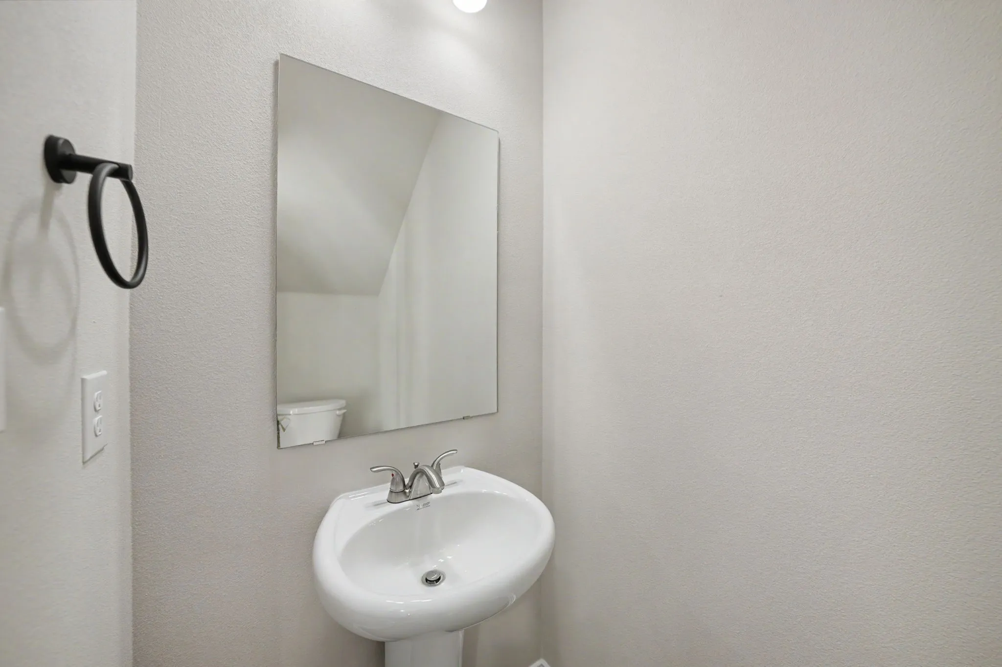 Pedestal sink with a chrome faucet, wall-mounted mirror, and a matte black towel ring
