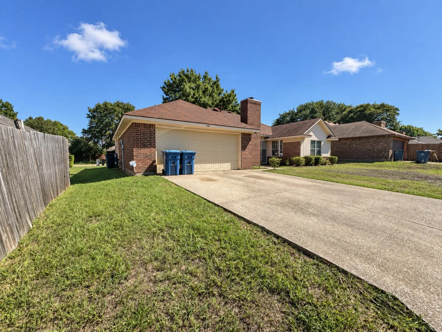 Brick exterior with a concrete driveway, attached garage, and a wood privacy fence