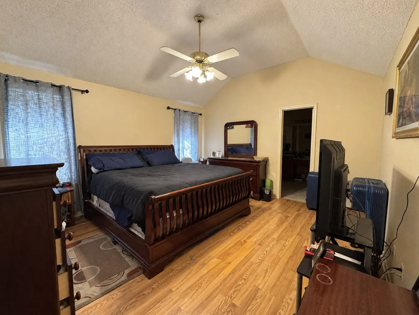 Vaulted ceiling with a ceiling fan light fixture, wood-finish flooring, and recessed doorway