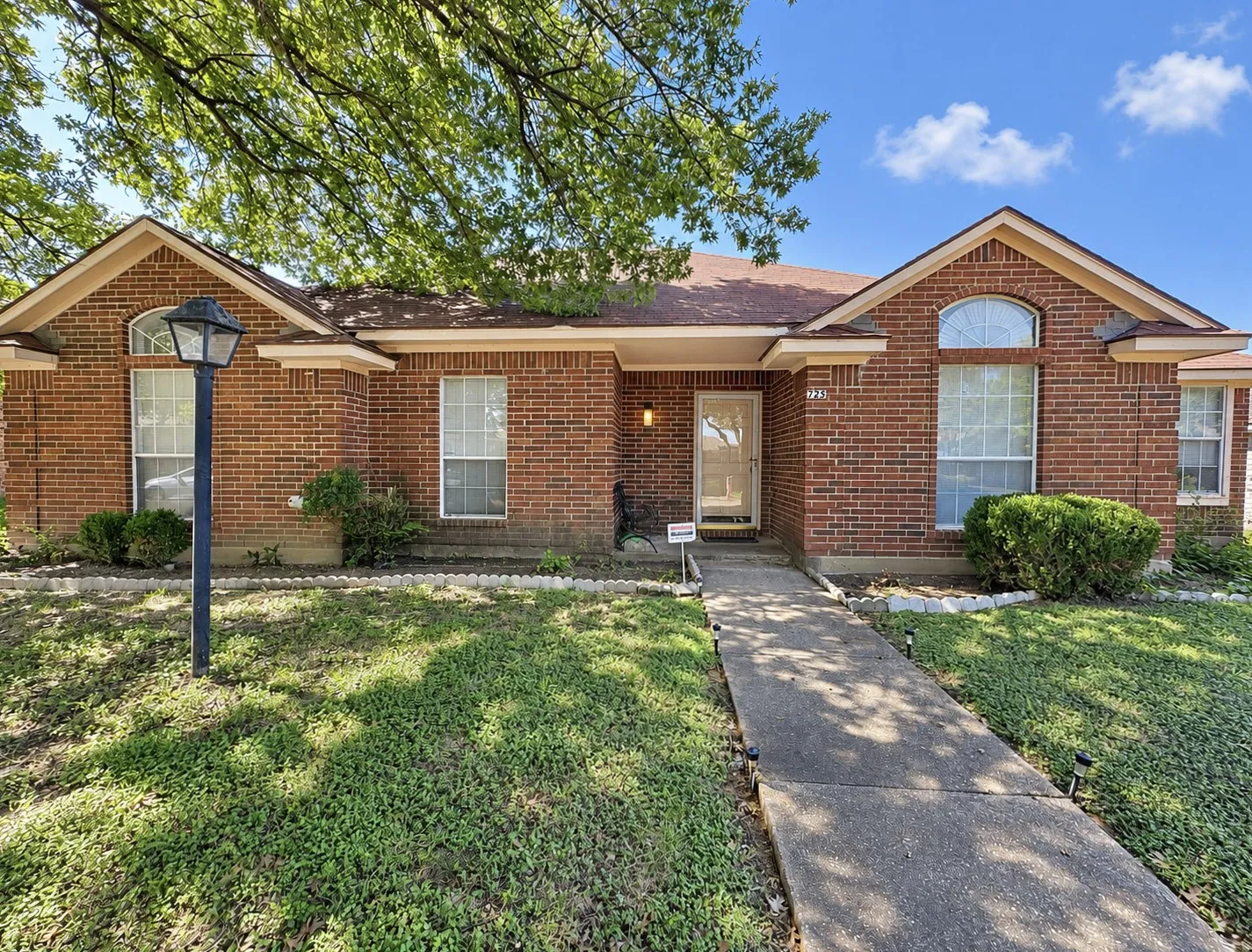 Brick exterior residence featuring a front entry, arched window, and mature landscaping