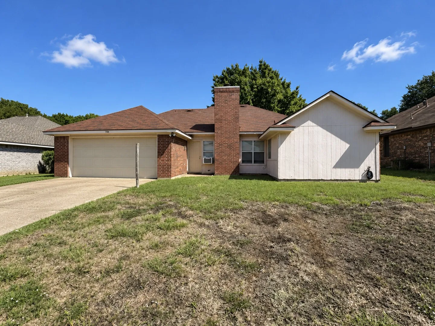 Brick and siding exterior with an attached garage, a chimney feature, and a paved driveway