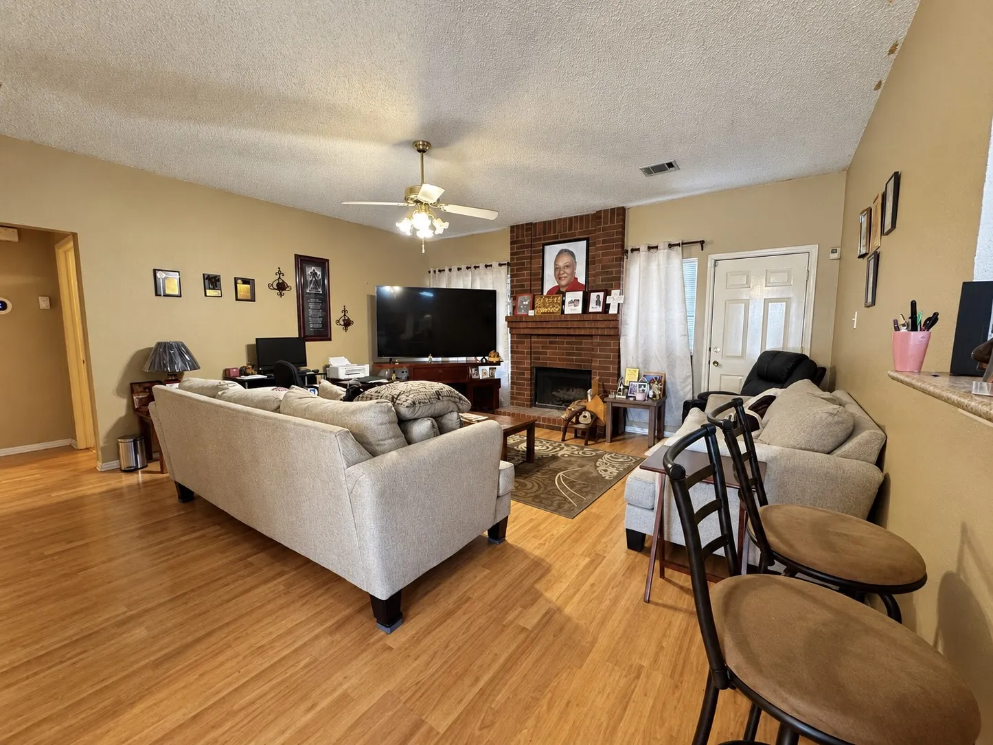 Wood-finish flooring throughout, brick-surround fireplace, ceiling fan with integrated lighting, and a white paneled door
