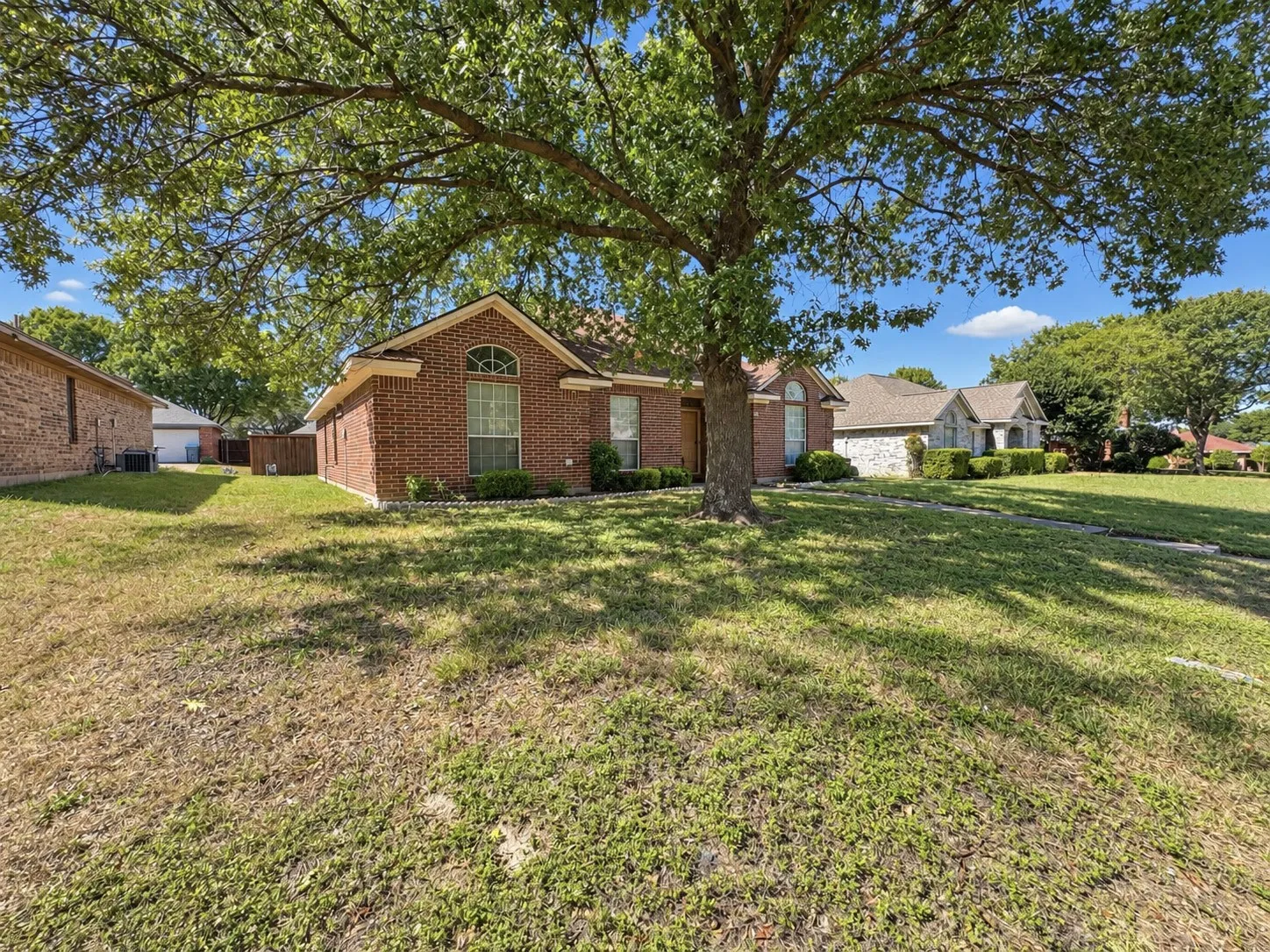 Brick-clad exterior with an arched window, a mature shade tree, and a pitched roof