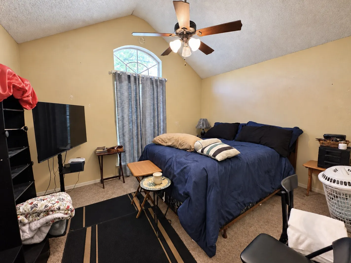 Vaulted ceiling with a ceiling fan, arched window, and carpeted flooring