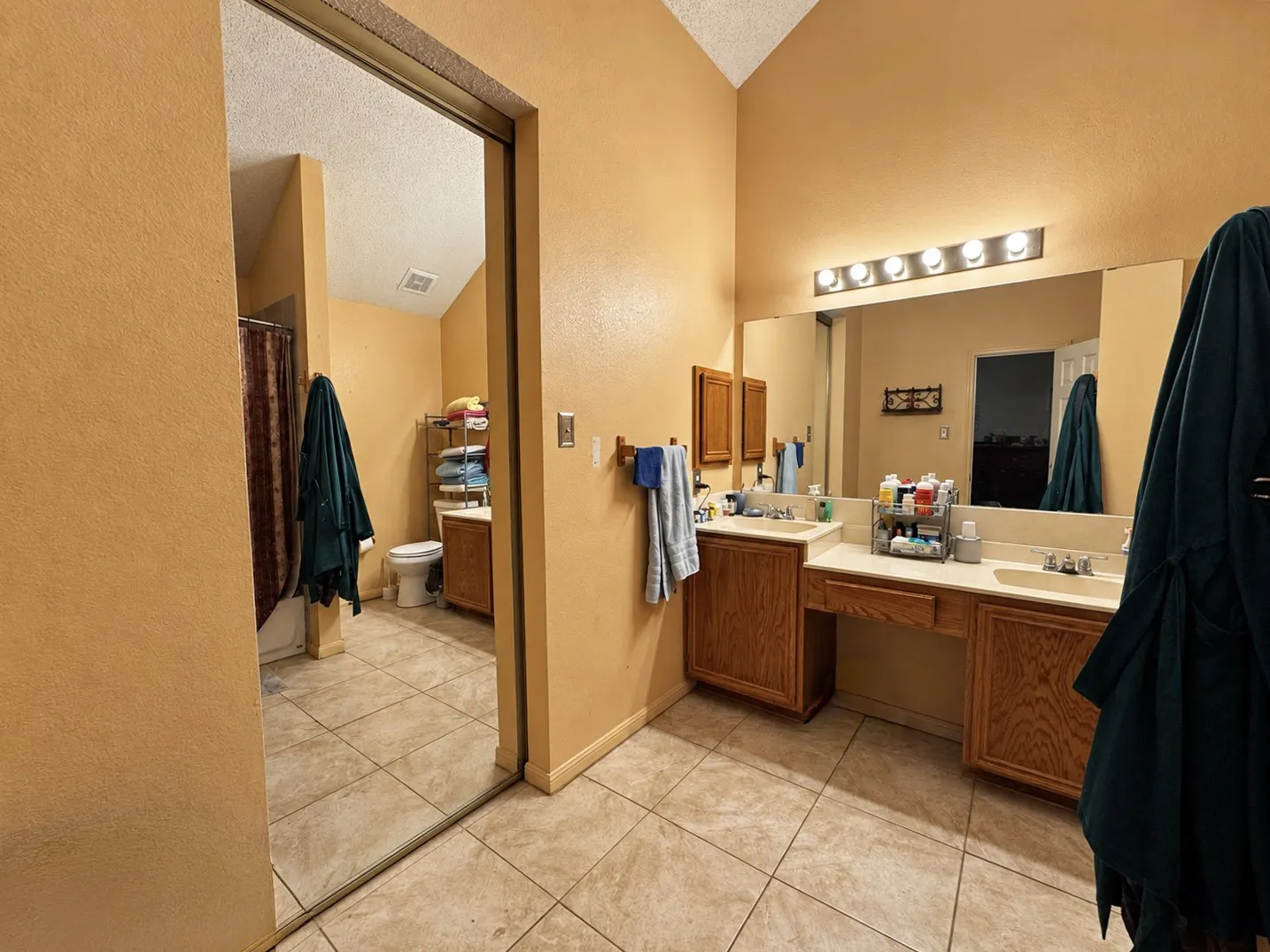 Vaulted ceiling bathroom featuring a dual vanity with oak-finish cabinetry, integrated sinks, and an expansive wall-mounted mirror
