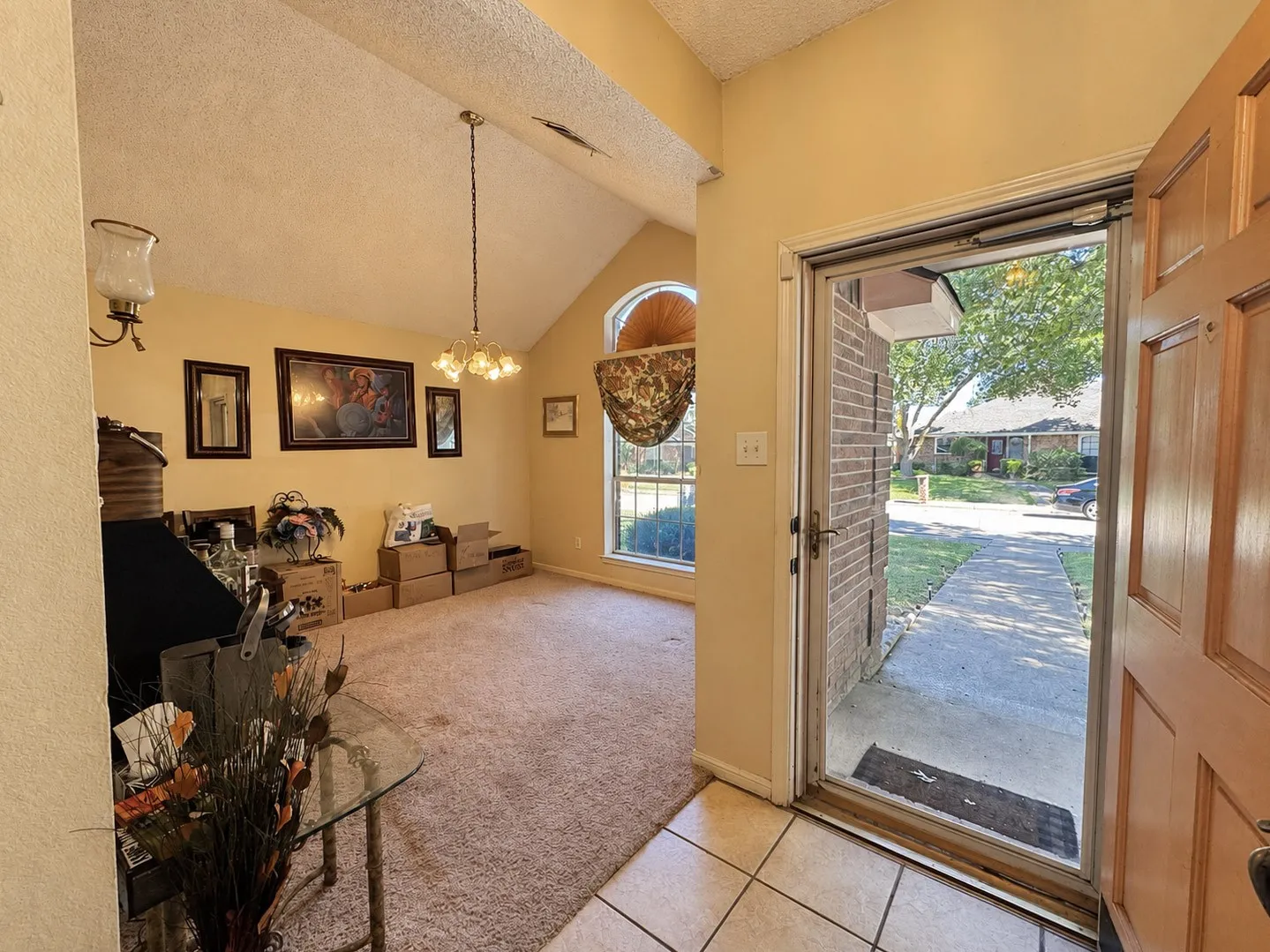 Vaulted ceiling, chandelier lighting, arched window, wood paneled door, and tile flooring at entrance