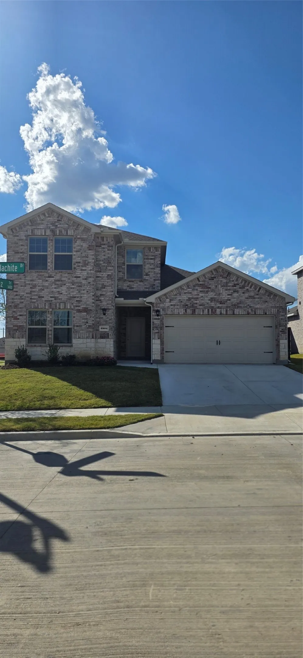 Two-story brick exterior with stone accents, attached two-car garage, concrete driveway, and a front lawn