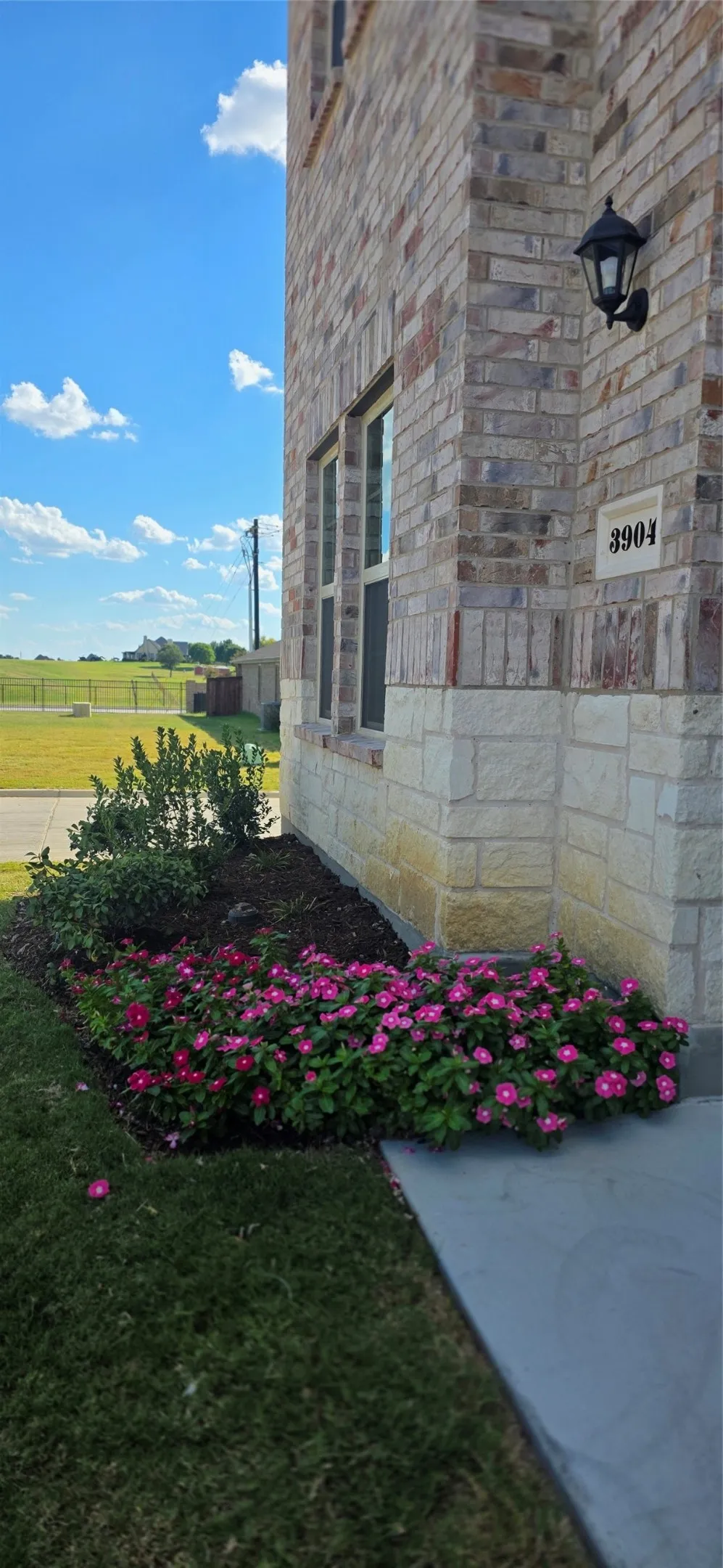Brick and stone facade featuring a decorative wall-mounted light fixture, address numbers, and ground-level landscaping
