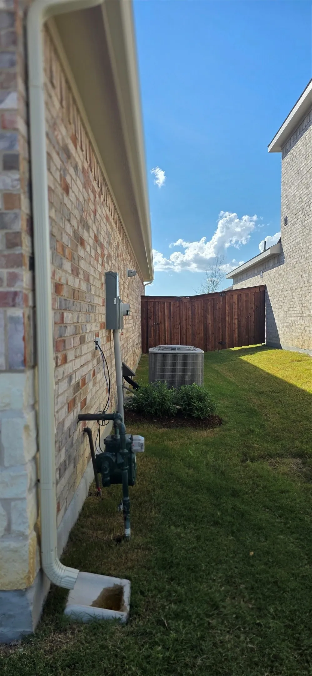 Brick and stone facade with a brown privacy fence, featuring a manicured lawn and an HVAC unit