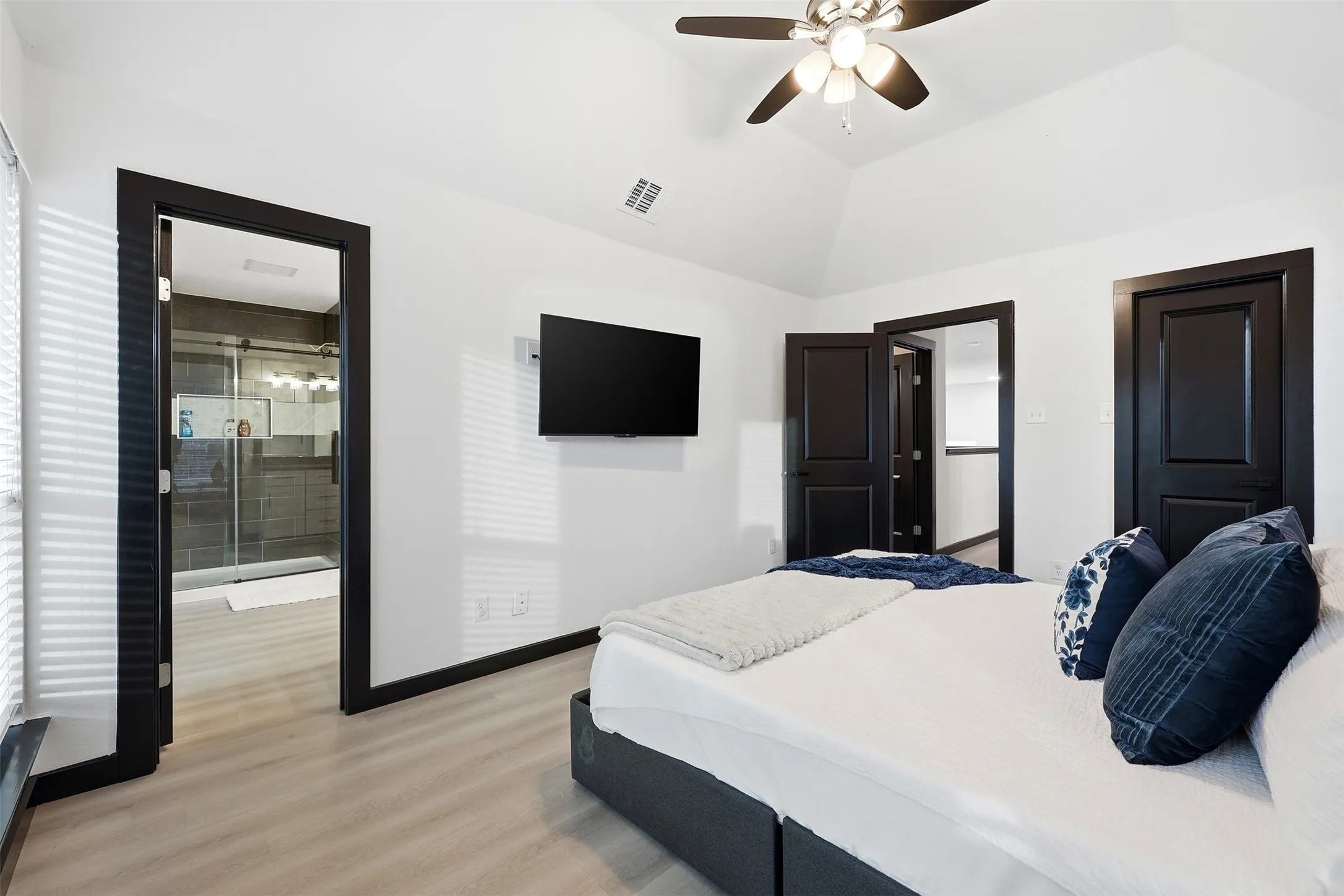 Vaulted ceiling with a ceiling fan, light wood-finish flooring, and dark trim doors