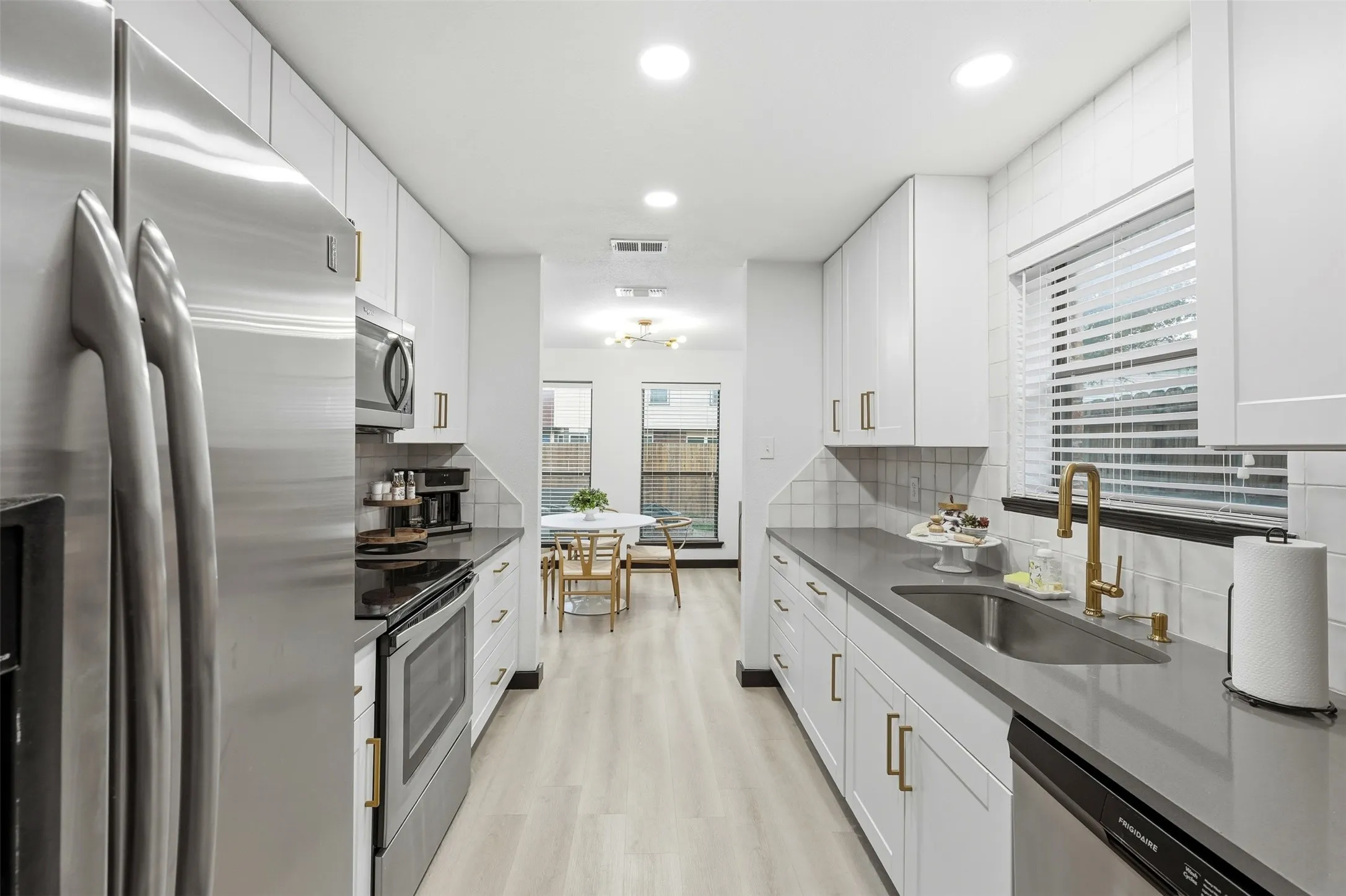 Galley kitchen featuring stainless steel appliances, light gray countertops, white cabinetry with gold-tone hardware, and wood-finish flooring