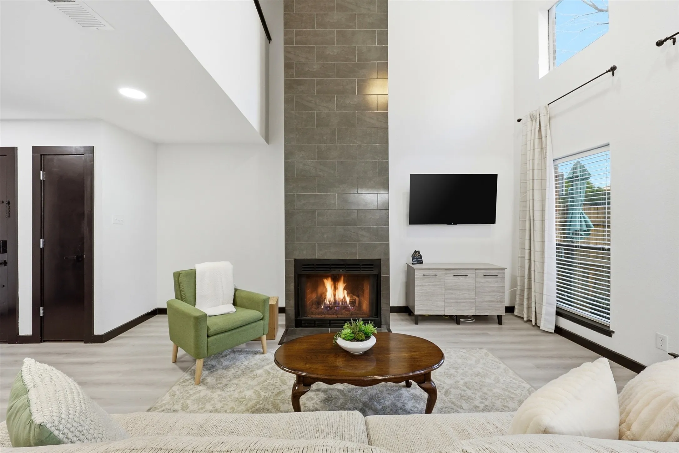 Soaring ceilings, a floor-to-ceiling tiled fireplace, and light wood-finish flooring define this living space