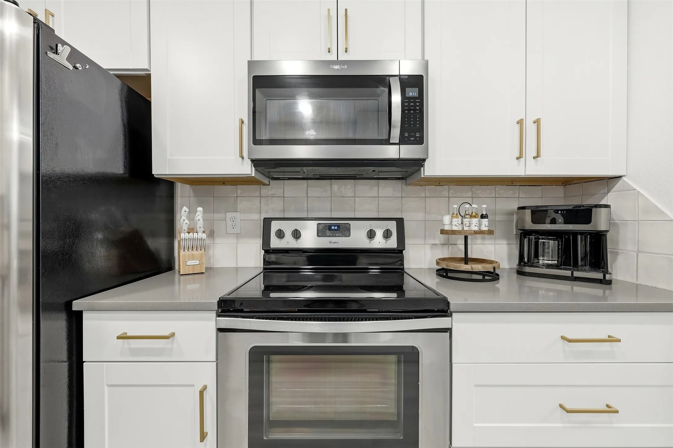 White cabinetry with gold-tone hardware, stainless steel appliances, and light-toned countertops