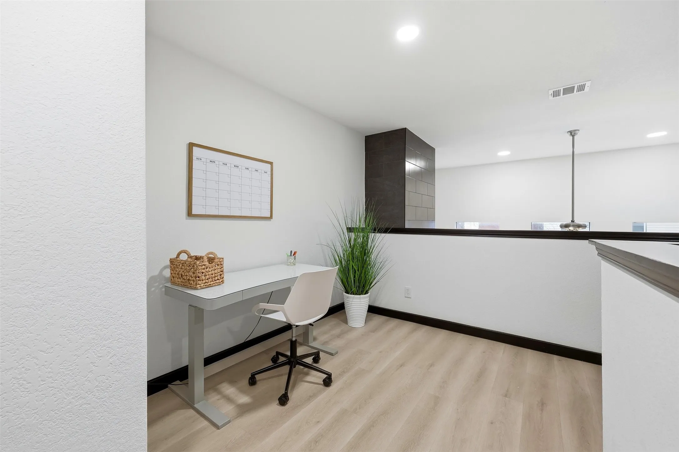Light wood-finish flooring, recessed ceiling lighting, and a dark tile-clad architectural element