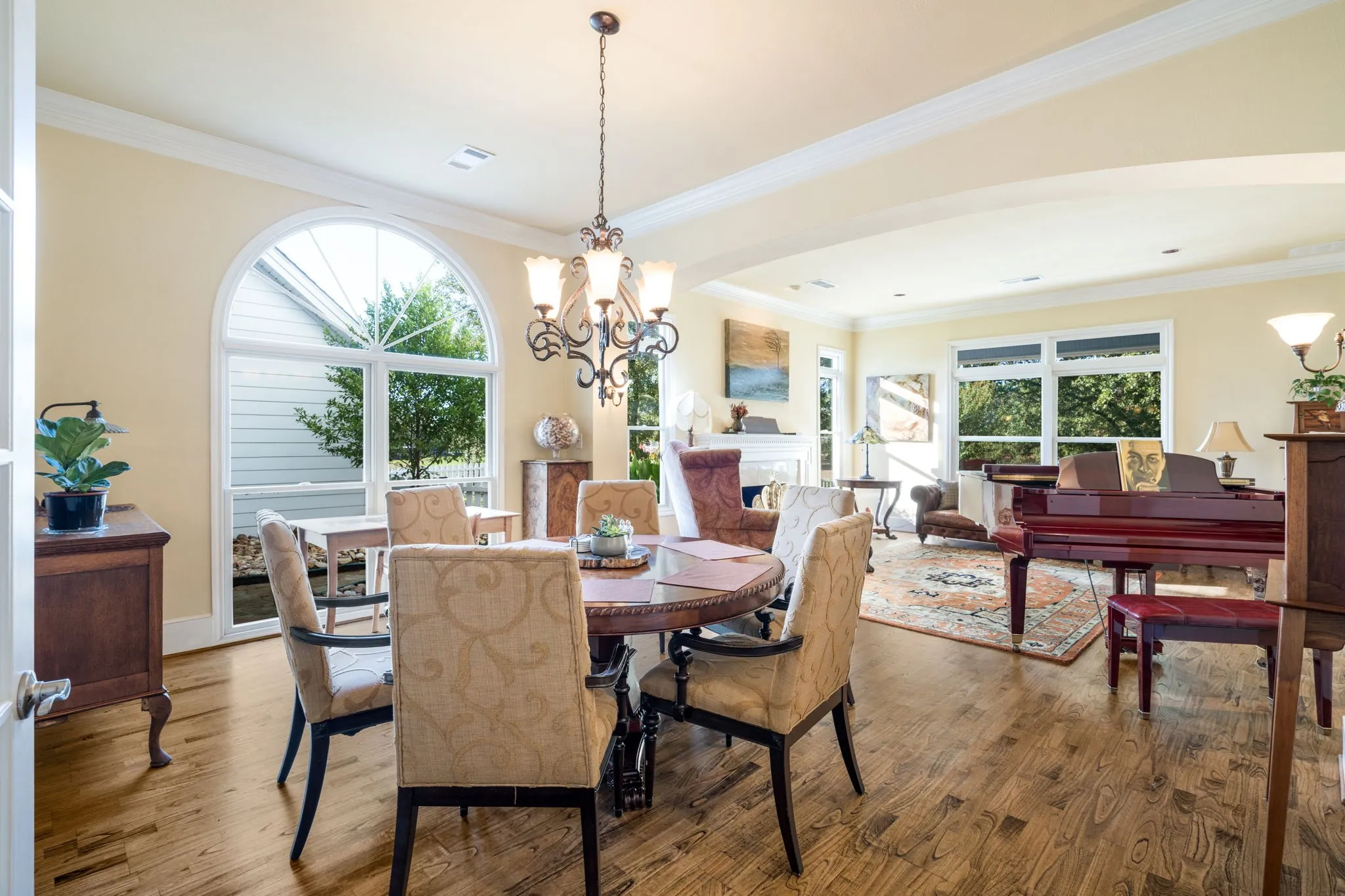 Wood-finish flooring throughout, featuring a large arched window, crown molding, and a chandelier with decorative glass shades
