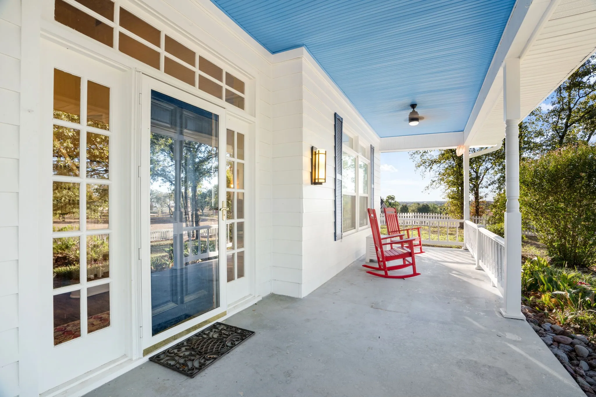 Expansive covered porch with a light blue beadboard ceiling, ceiling fan, and outdoor wall sconce