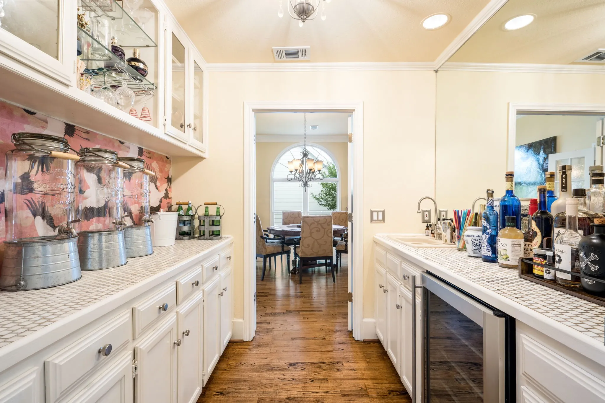 Expansive butler's pantry featuring glass-front upper cabinetry, white lower cabinetry, a built-in beverage refrigerator, and a stainless steel sink with a gooseneck faucet