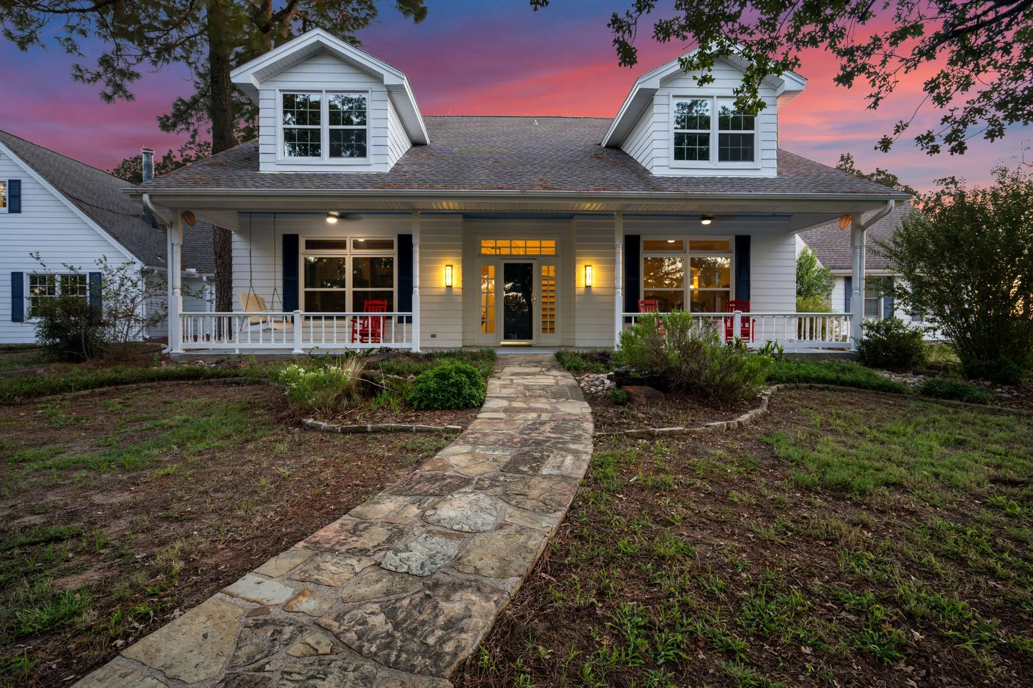 White siding exterior with black shutters, dormer windows, covered front porch, and a stone-paver walkway