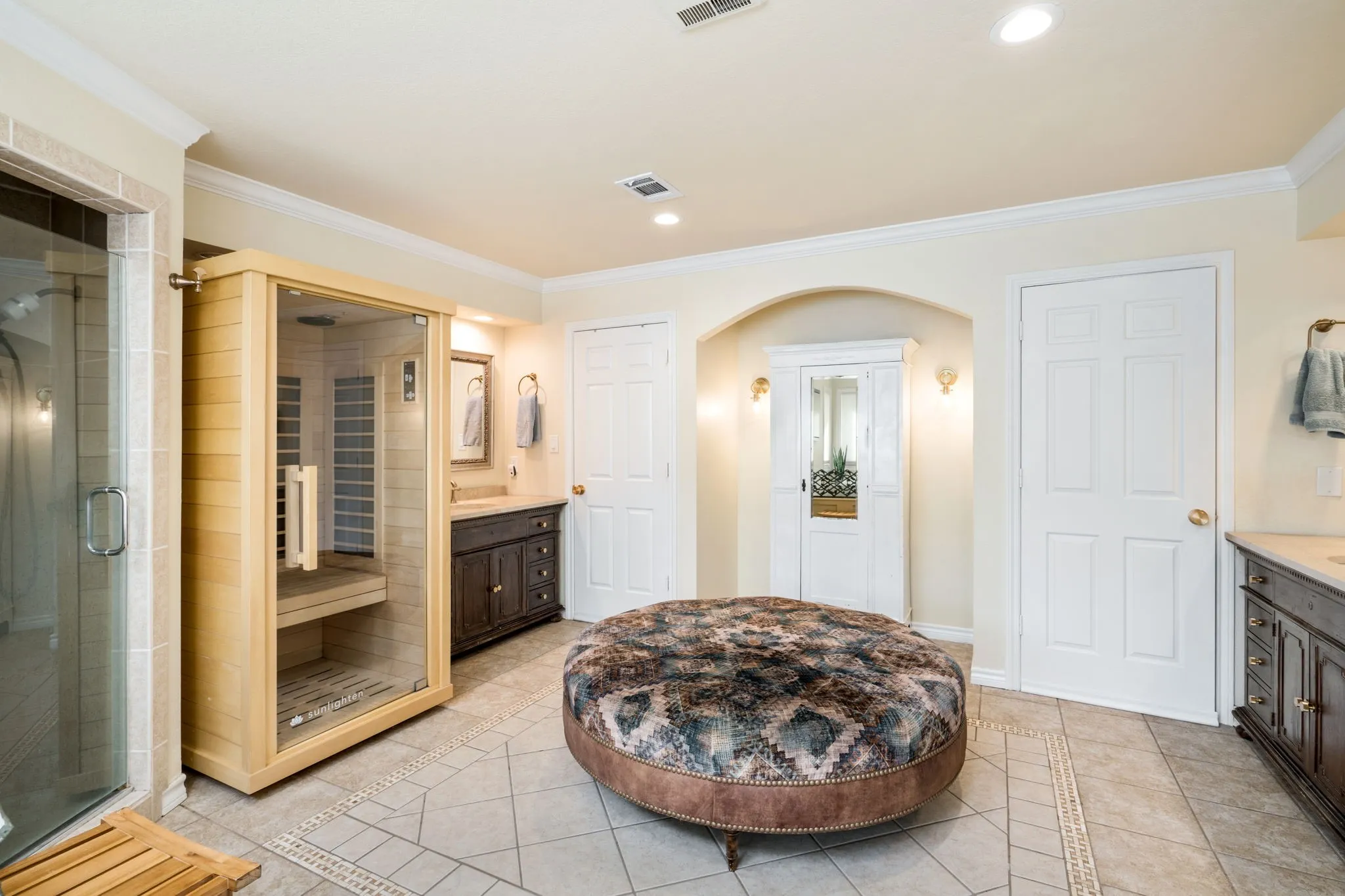 Built-in sauna, glass-enclosed shower, dual vanity sinks, arched wall niche, and tile flooring with decorative inlay