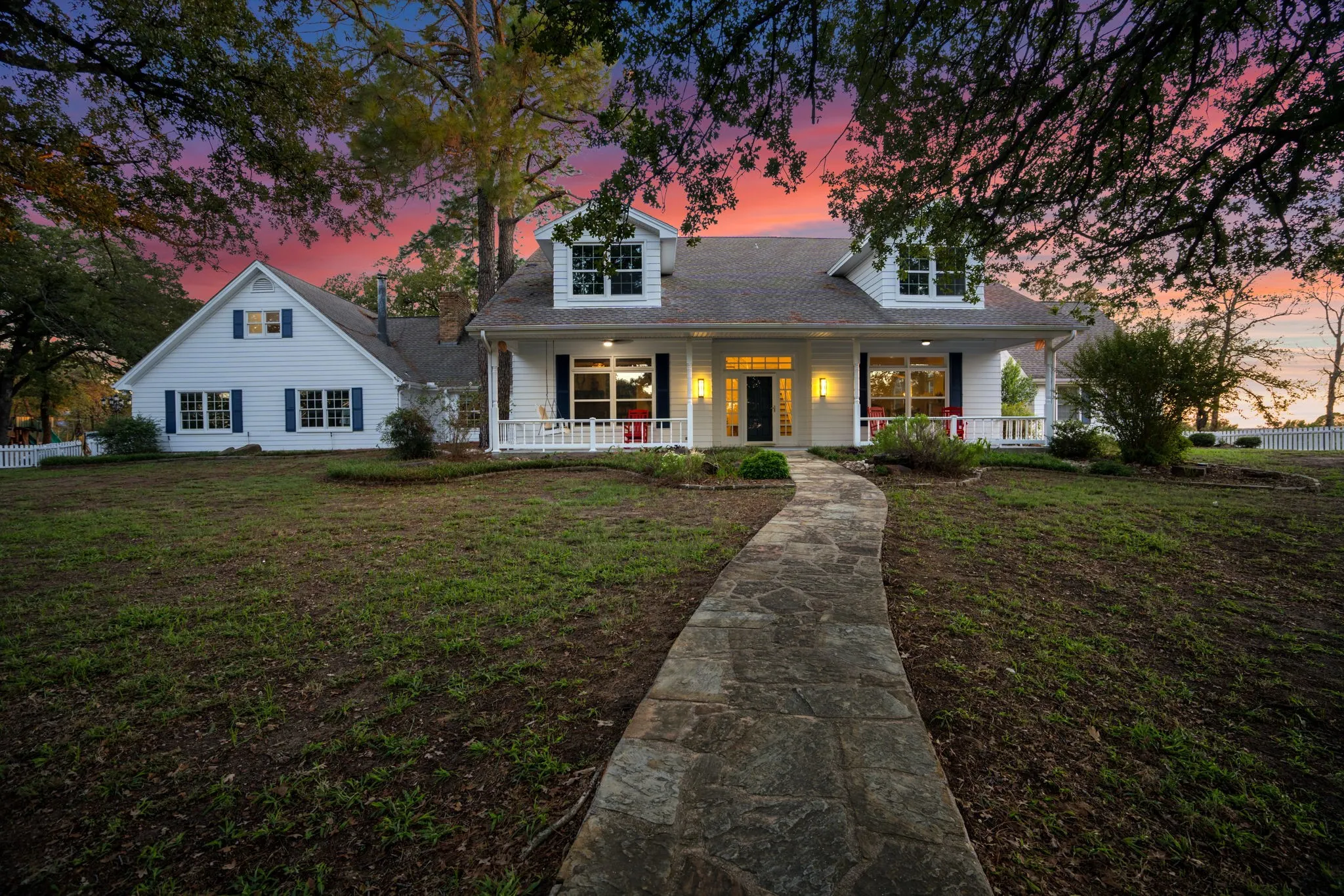 White siding residence featuring multiple dormer windows, a covered front porch with white railing, and a flagstone pathway