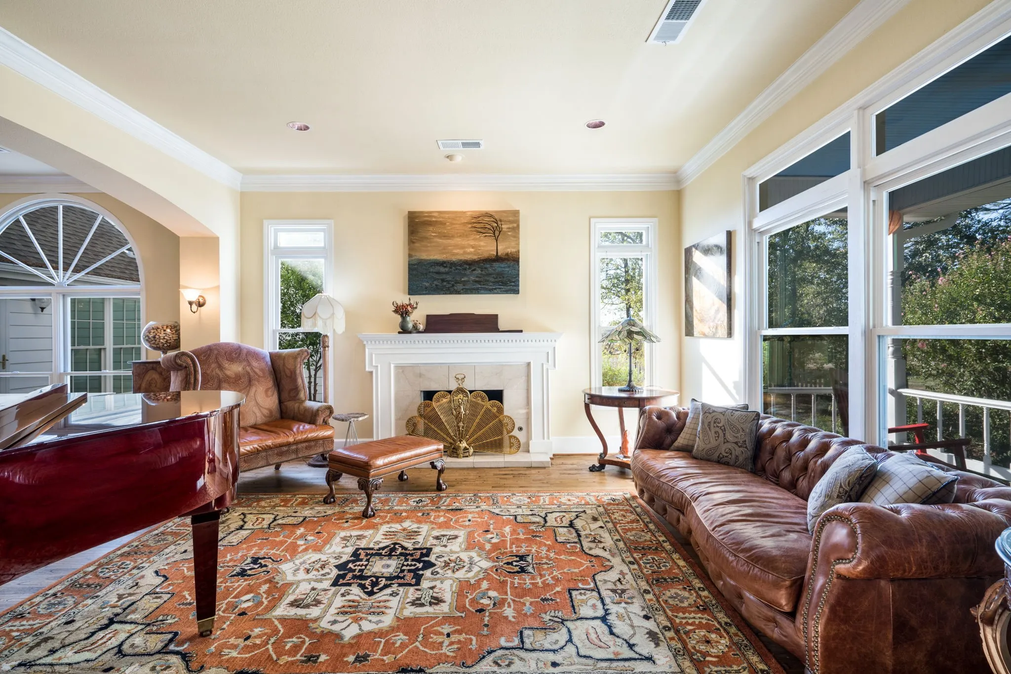 Spacious living area featuring hardwood flooring, a white mantel fireplace, extensive crown molding, a large arched window, and tall windows