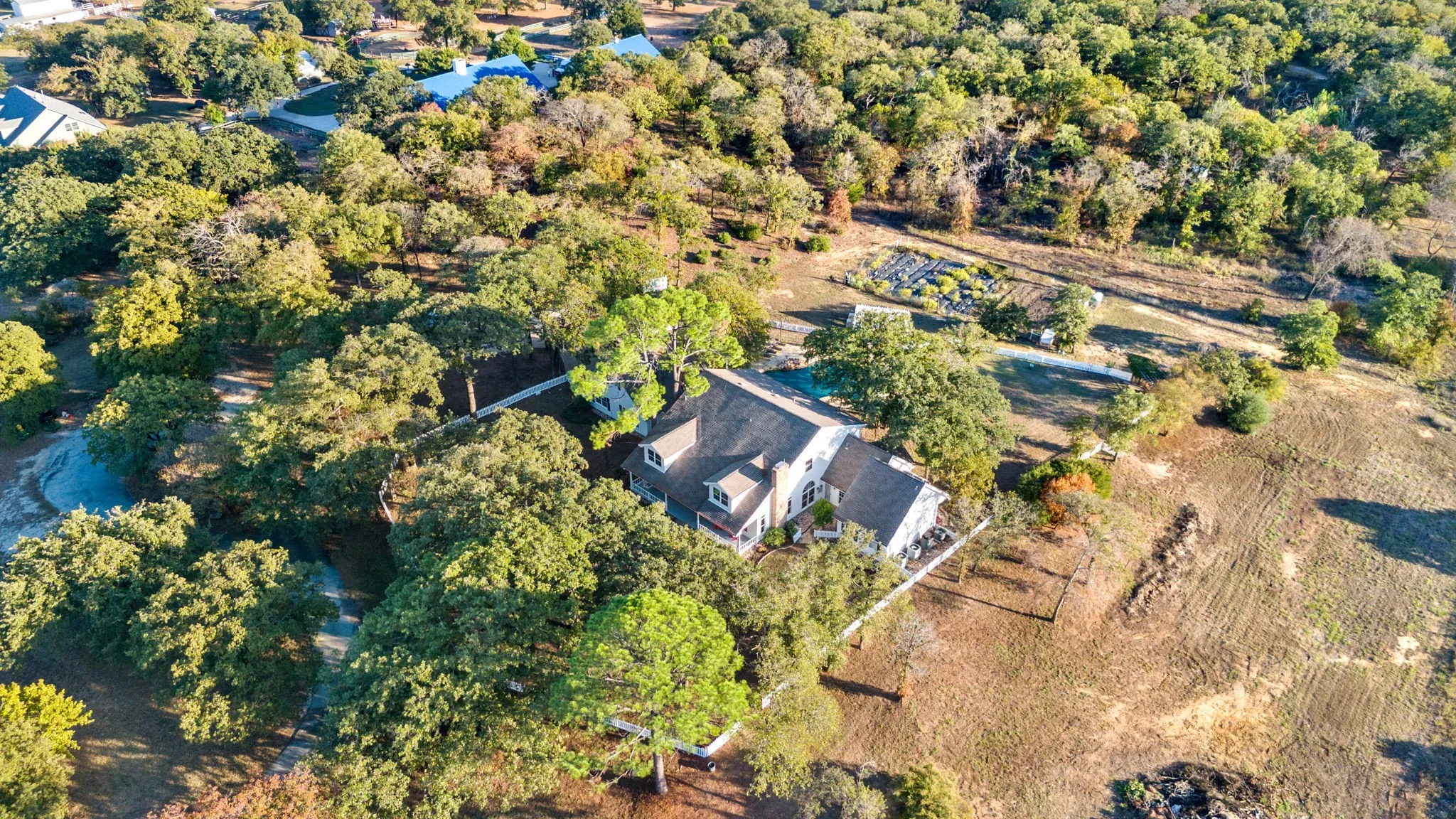 Expansive property surrounded by mature trees, featuring a multi-story residence with a gabled roof and covered porch