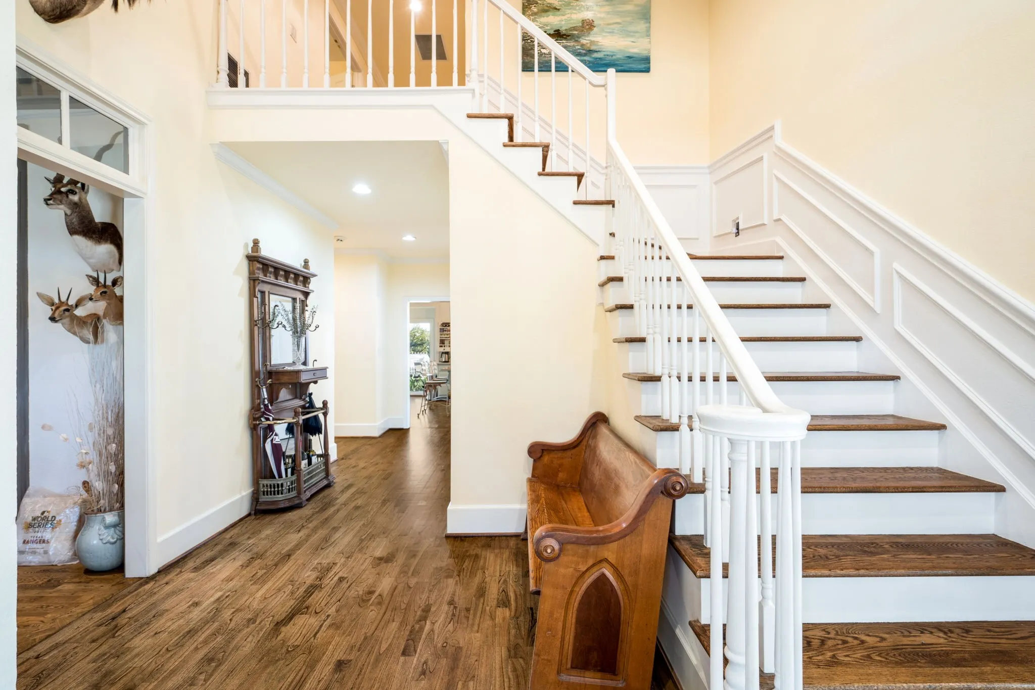 Two-story foyer with wood-finish flooring, staircase with white risers and wood-finish treads, and white wainscoting